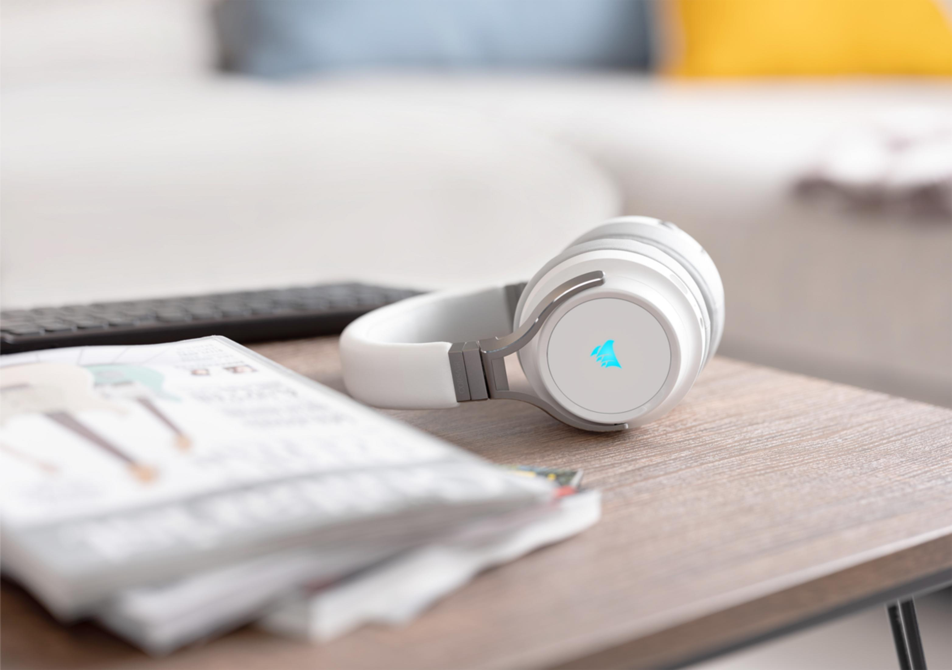 Auriculares blancos con logo azul sobre mesa de madera junto a revistas.