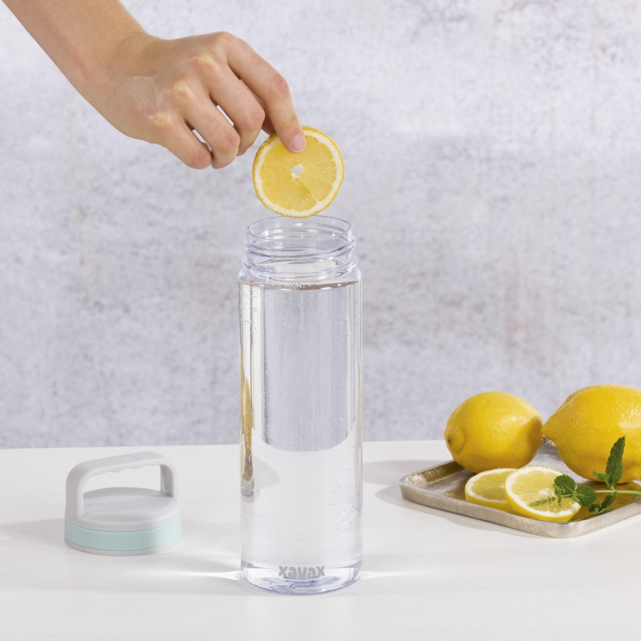 Eine Hand lässt eine Zitronenscheibe in eine klare Flasche mit Wasser fallen.