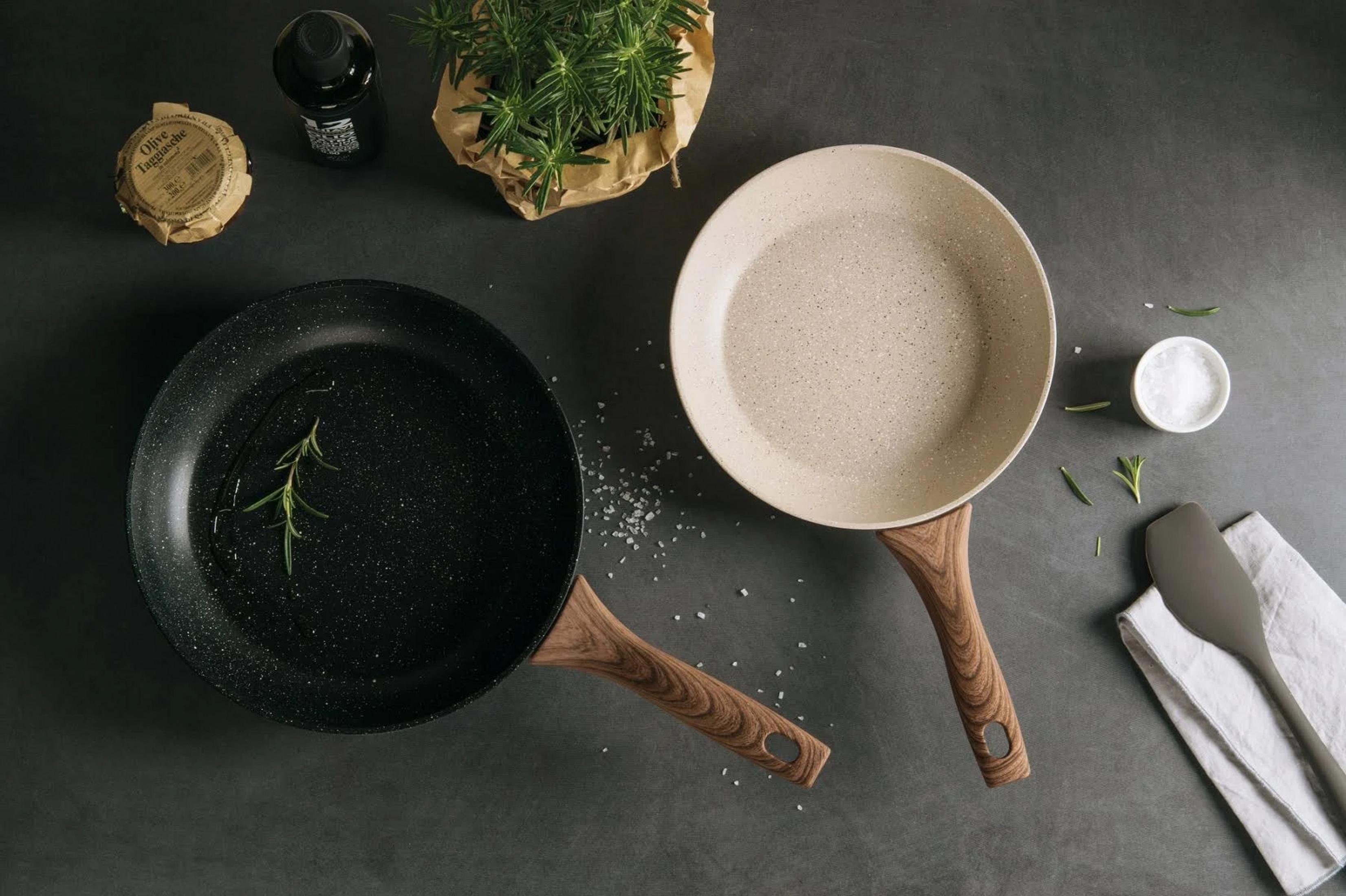 Deux poêles avec manches en bois, herbes et sel sur fond sombre.