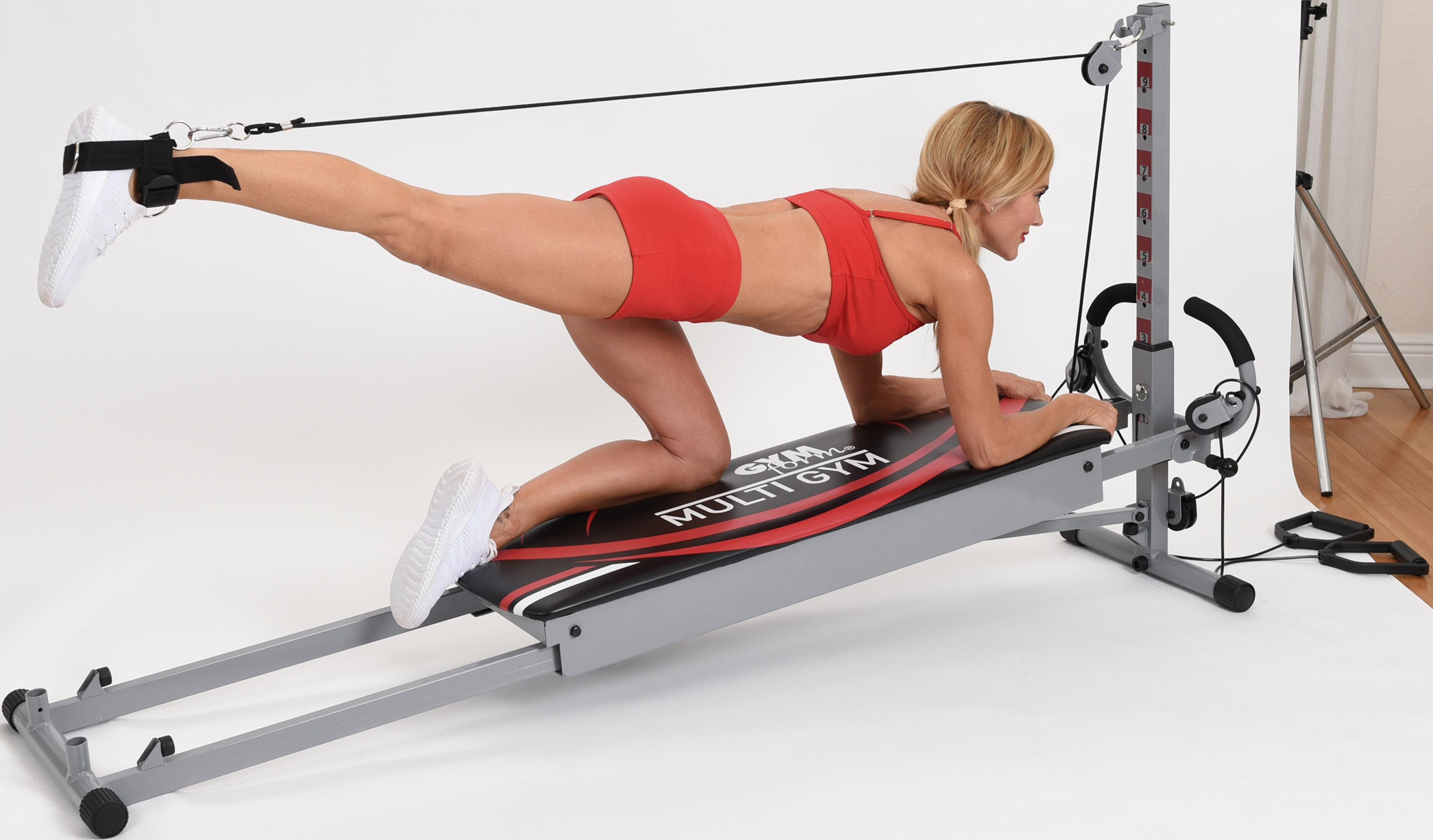 Frau auf Fitnessgerät, ein Bein angehoben, in rotem Sport-BH und Shorts.