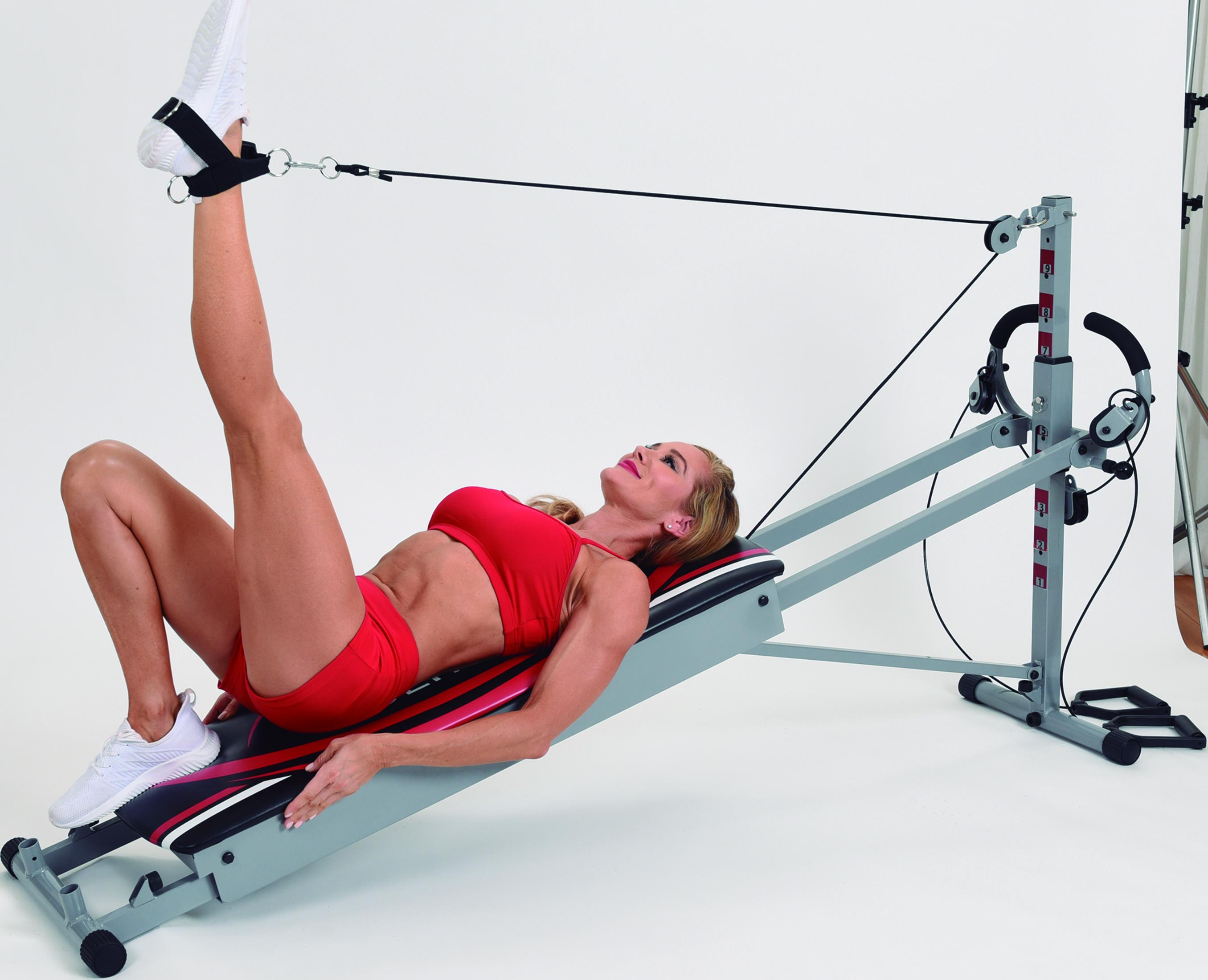 Eine Frau in roter Sportkleidung trainiert mit einem Heimtrainer auf einer Liege.