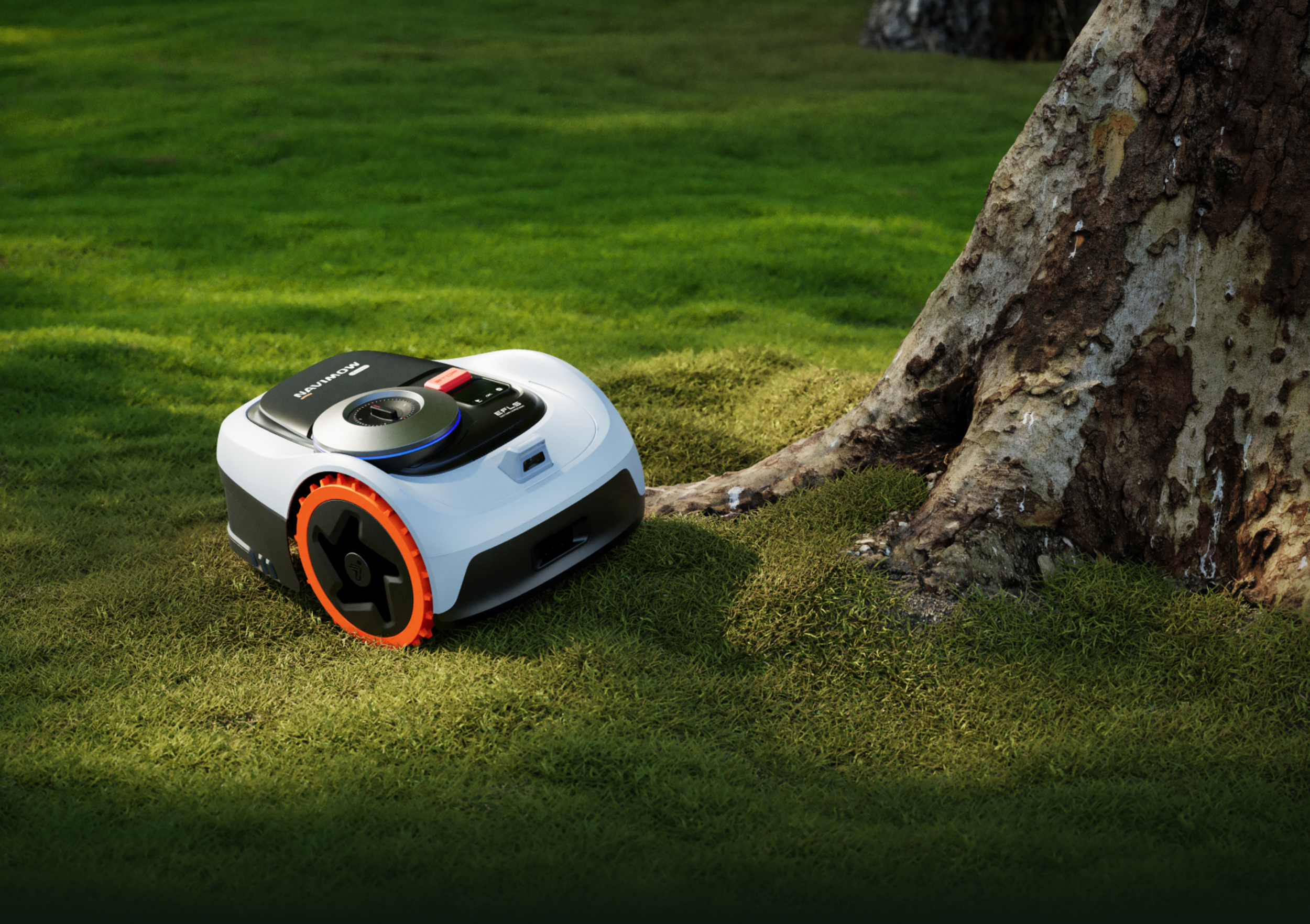Ein weißer Mähroboter mit orangen Rädern steht auf einem Rasen neben einem Baum.