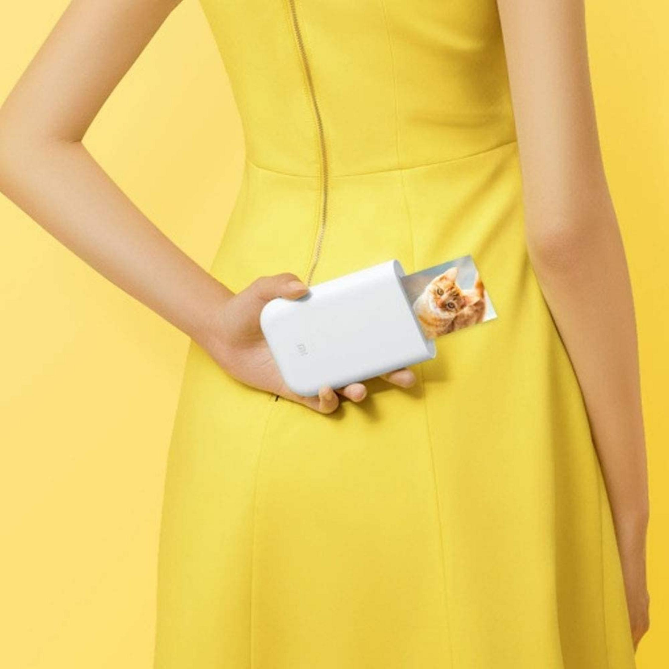 Una caja de impresora de fotos blanca con una imagen de gato es sostenida por una persona con un vestido amarillo.