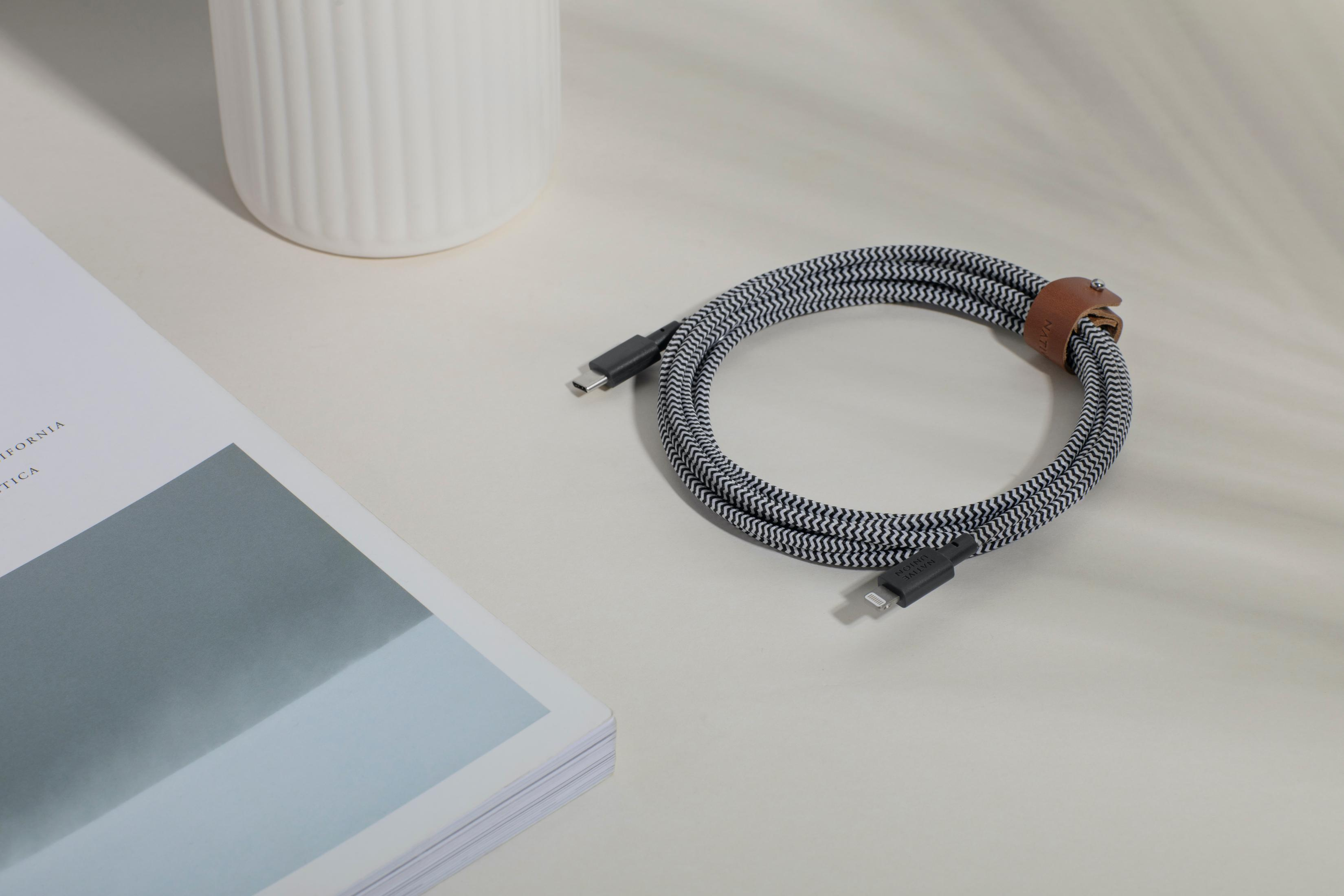 Un cavo di ricarica a righe bianche e nere con connettori USB-C e Lightning è su un tavolo.