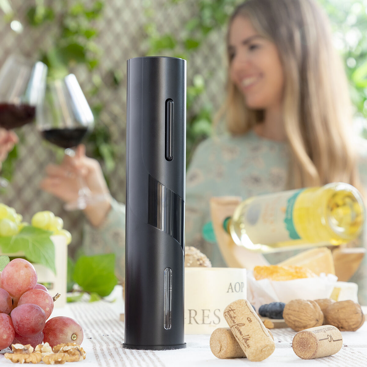 Un sacacorchos eléctrico negro en una mesa con uvas, queso y vino.