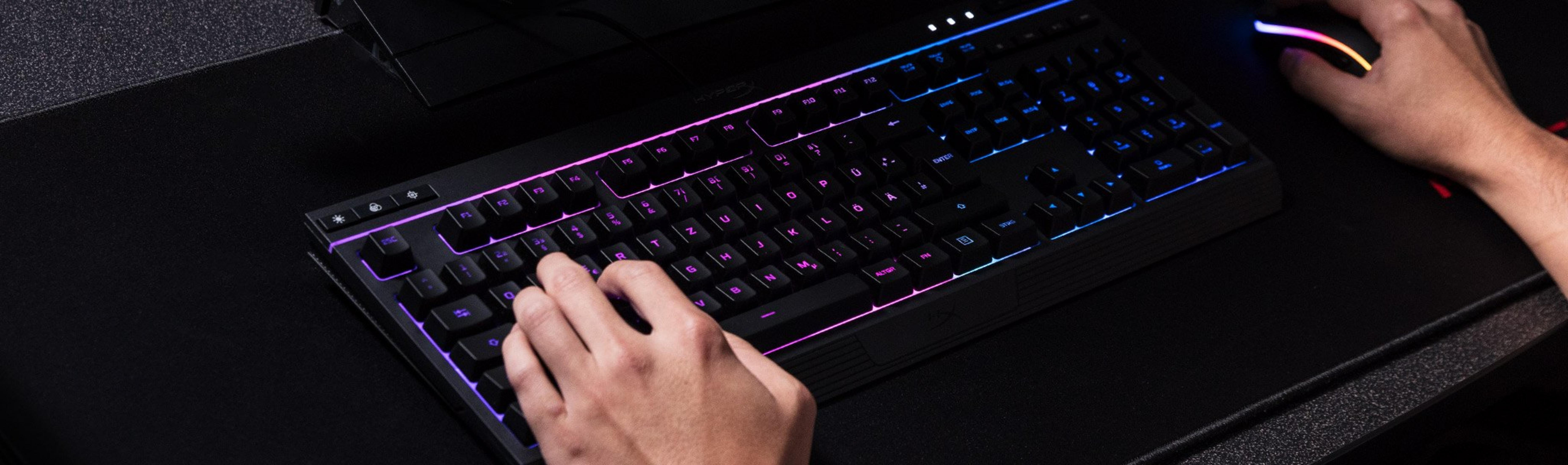 Eine Person tippt auf einer schwarz beleuchteten Tastatur mit RGB-Lichteffekten.