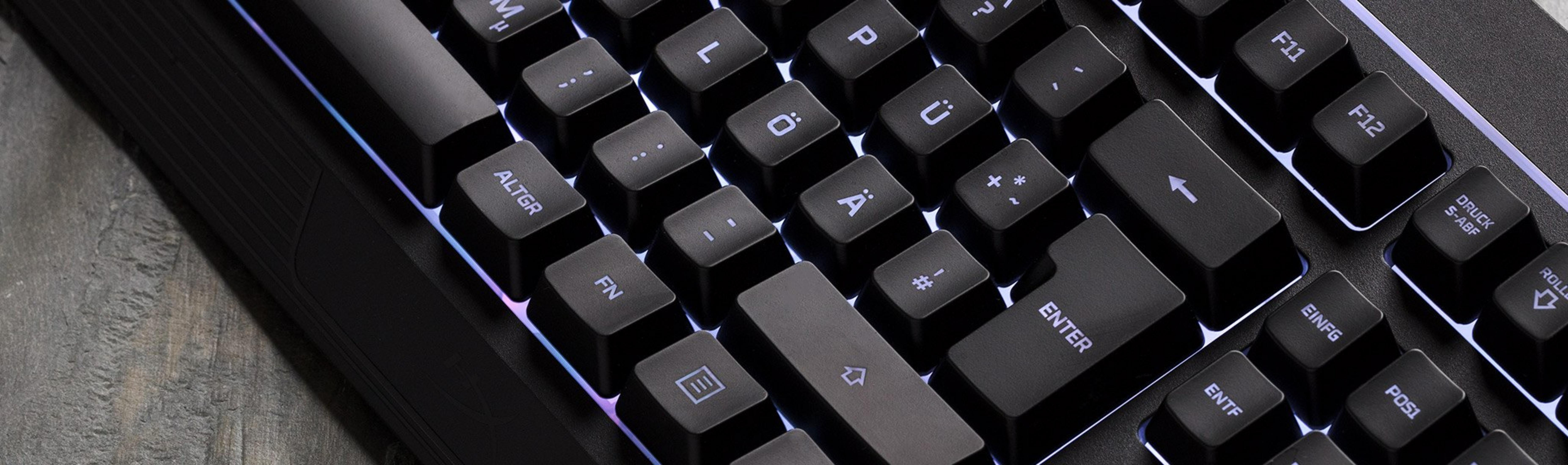 Eine Nahaufnahme einer schwarzen Tastatur mit RGB-Beleuchtung, die auf einem Holztisch liegt.