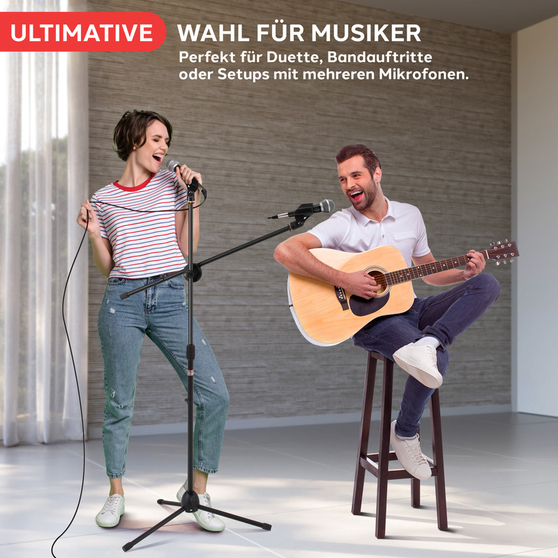 Frau singt ins Mikrofon, Mann spielt Gitarre auf Hocker. Musikszene.