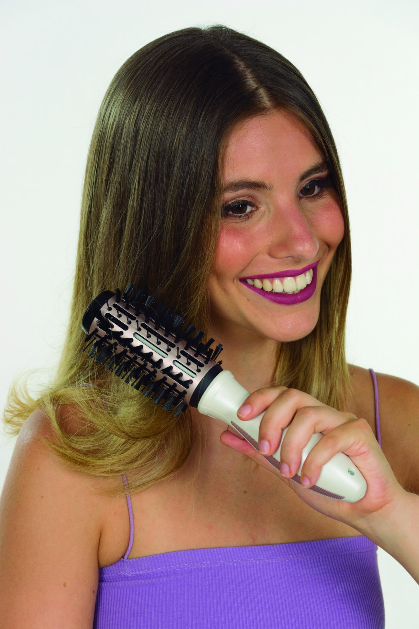 Donna con rossetto viola si acconcia i capelli biondi con una spazzola rotonda.