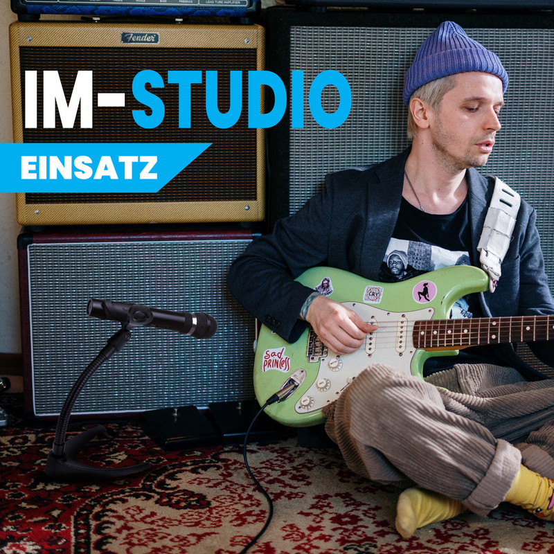 Ein Mann mit blauem Hut spielt E-Gitarre in einem Studio vor Gitarrenverstärkern.
