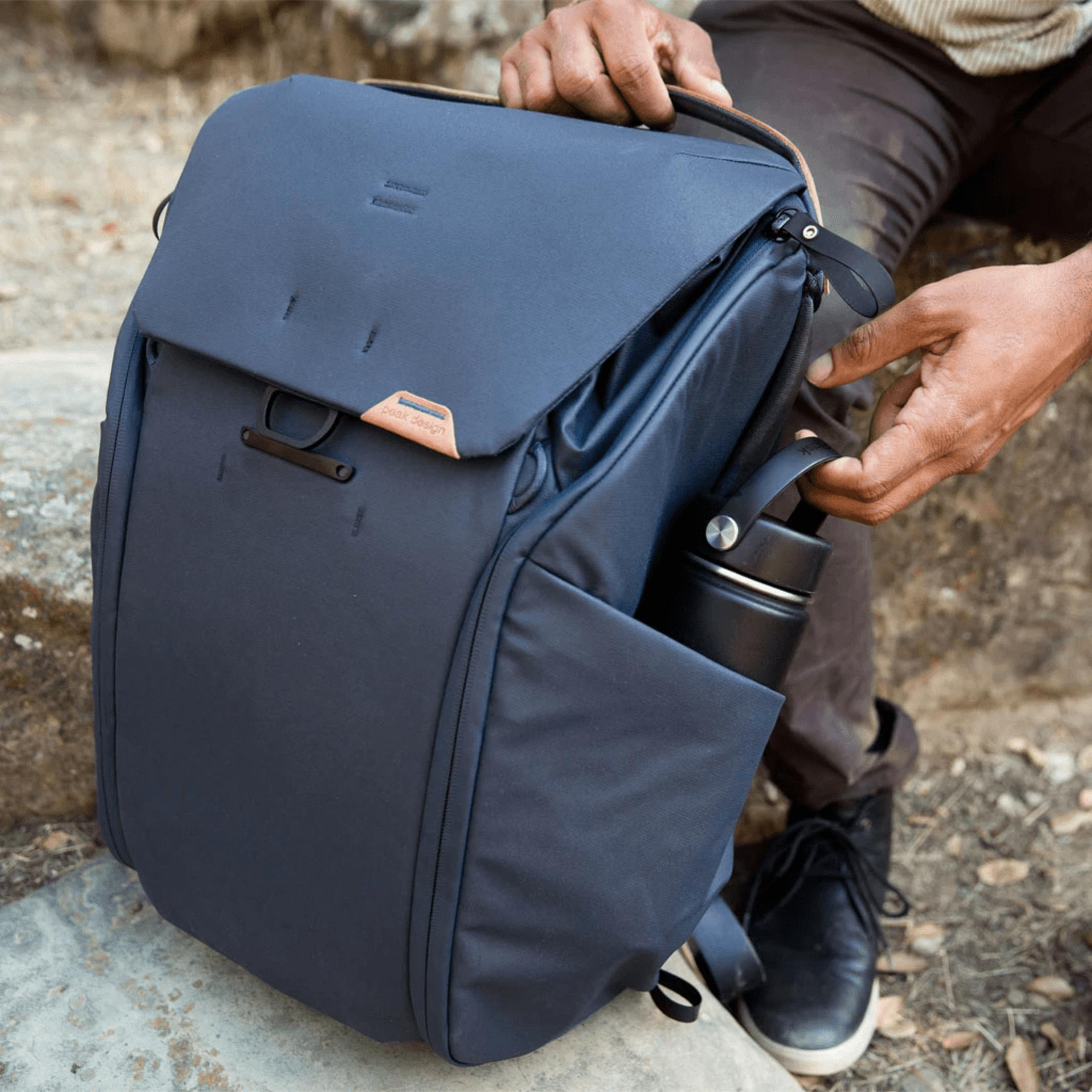 Dunkelgrauer Rucksack mit Lederdetails, daneben eine schwarze Wasserflasche.