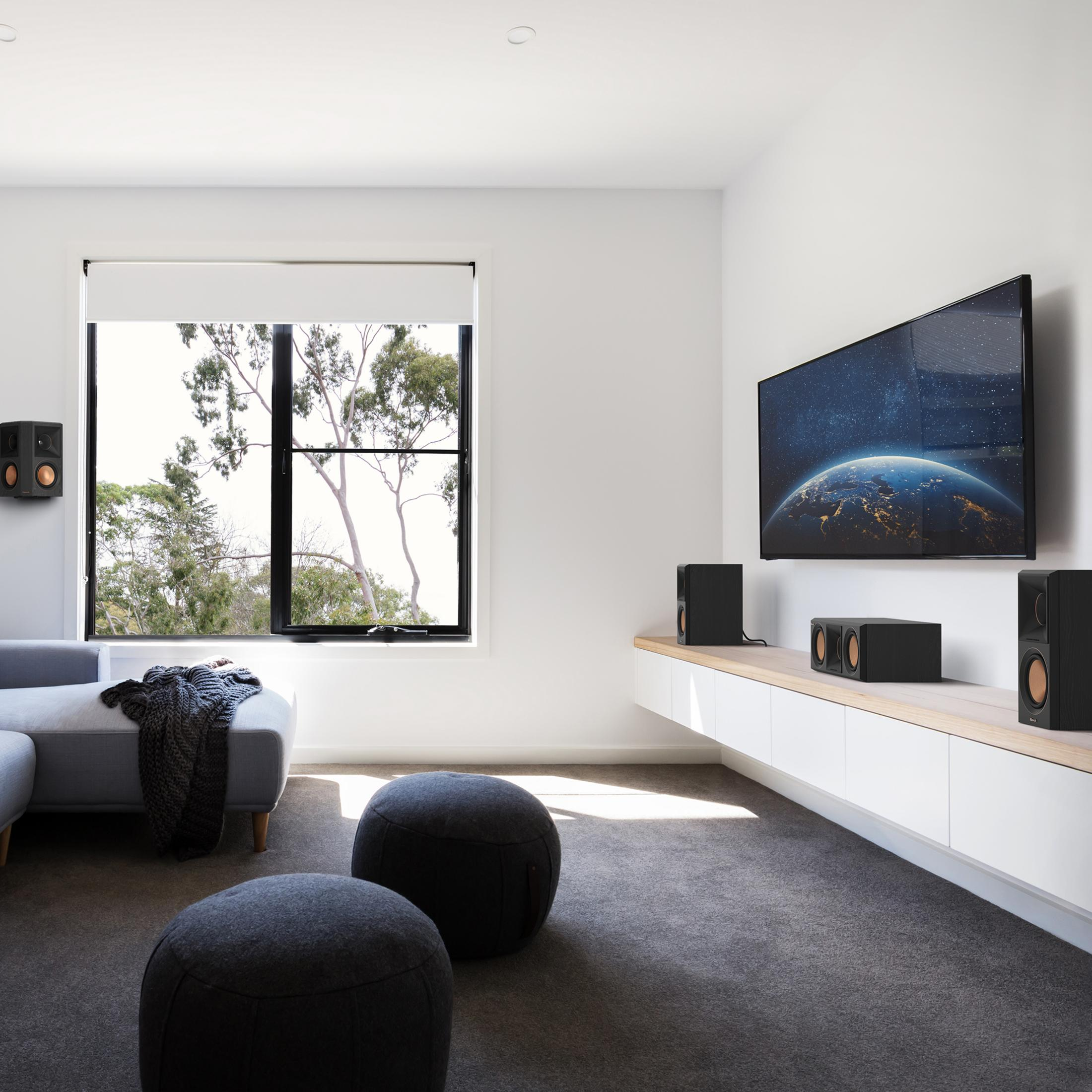 Ein Wohnzimmer mit einem grauen Sofa, zwei Poufs, einem Fernseher mit Erdbild und Lautsprechern.