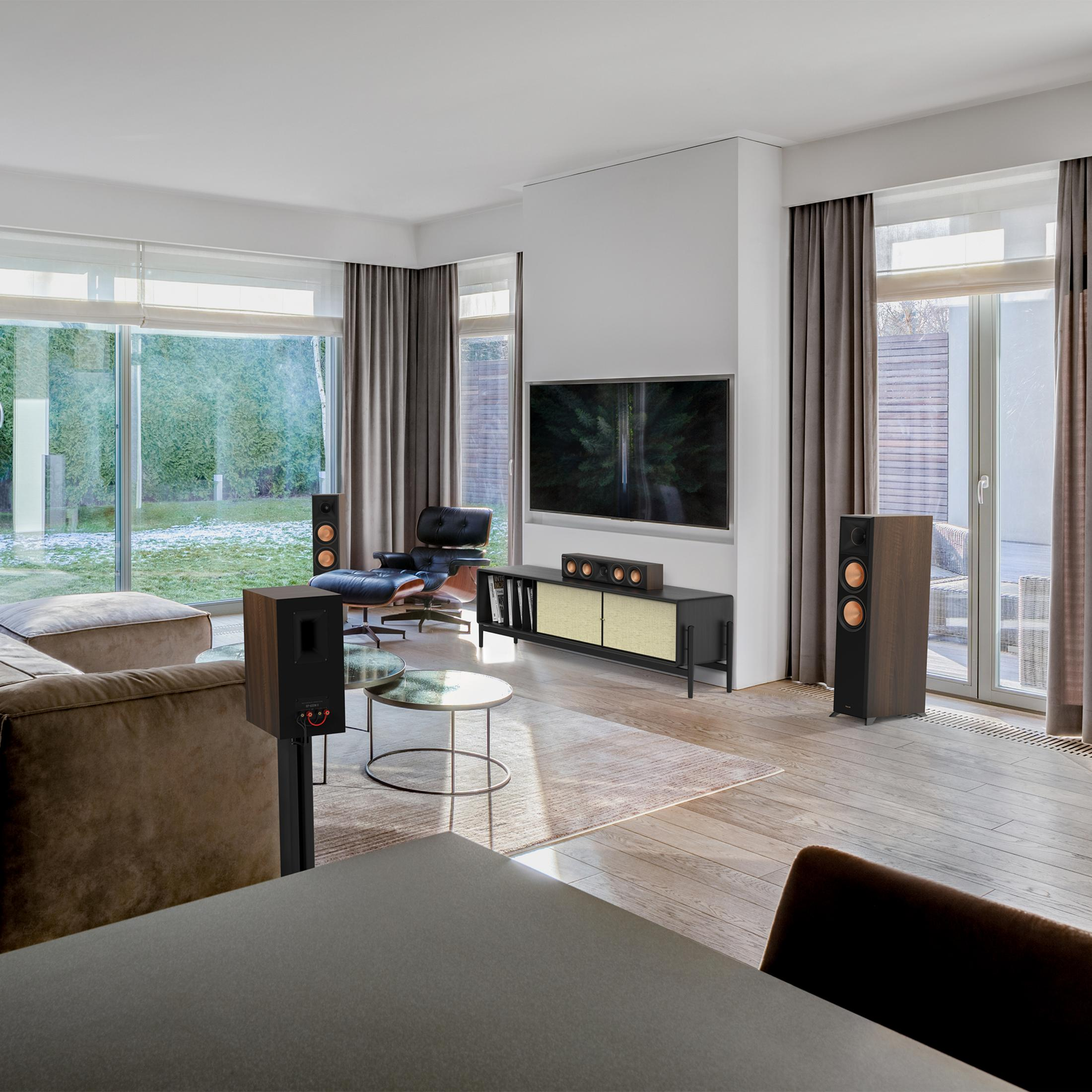 Modernes Wohnzimmer mit brauner Couch, schwarzem Ledersessel, Fernseher und Lautsprechern.