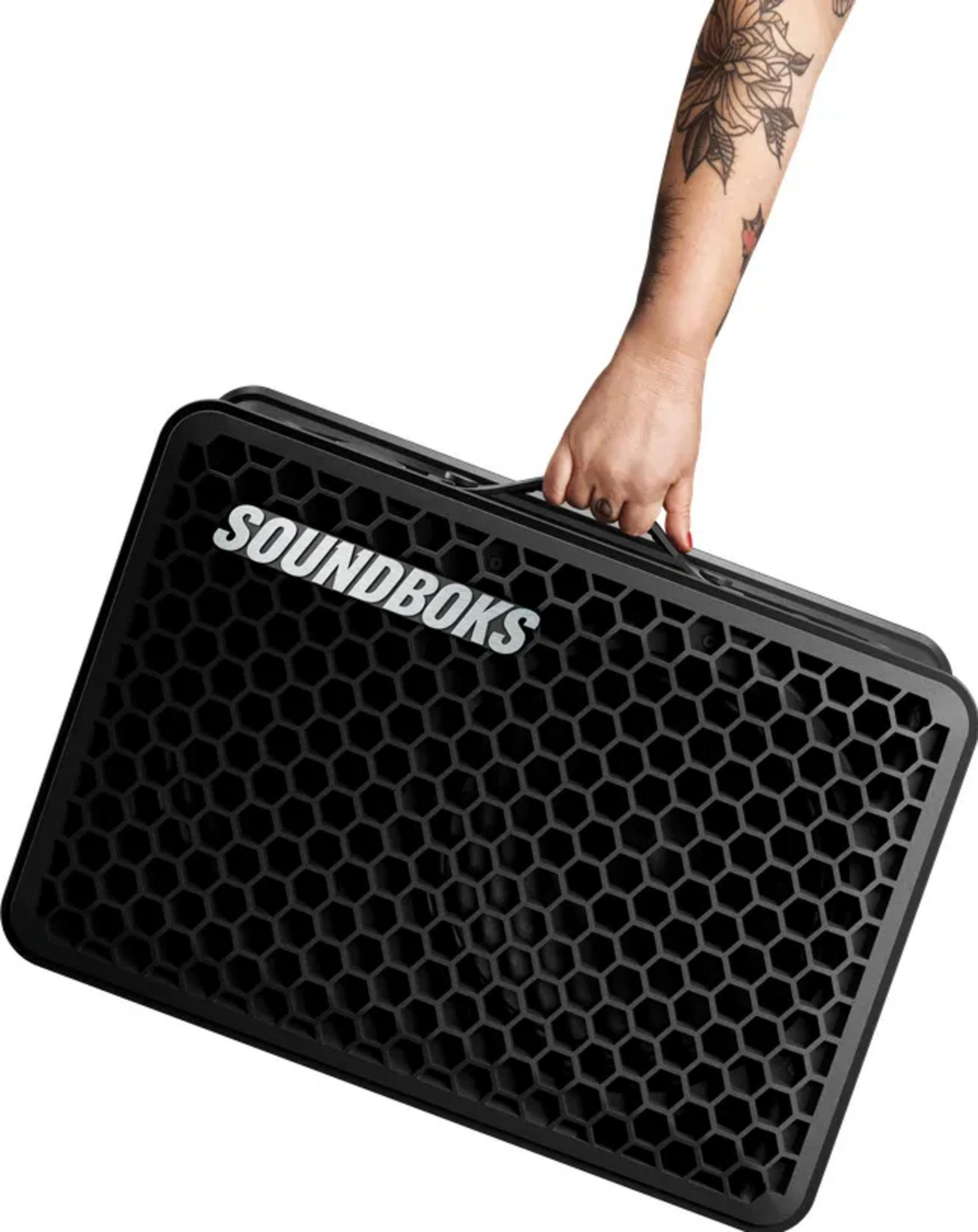 Eine Person mit tätowiertem Arm trägt eine schwarze SOUNDBOKS-Box.