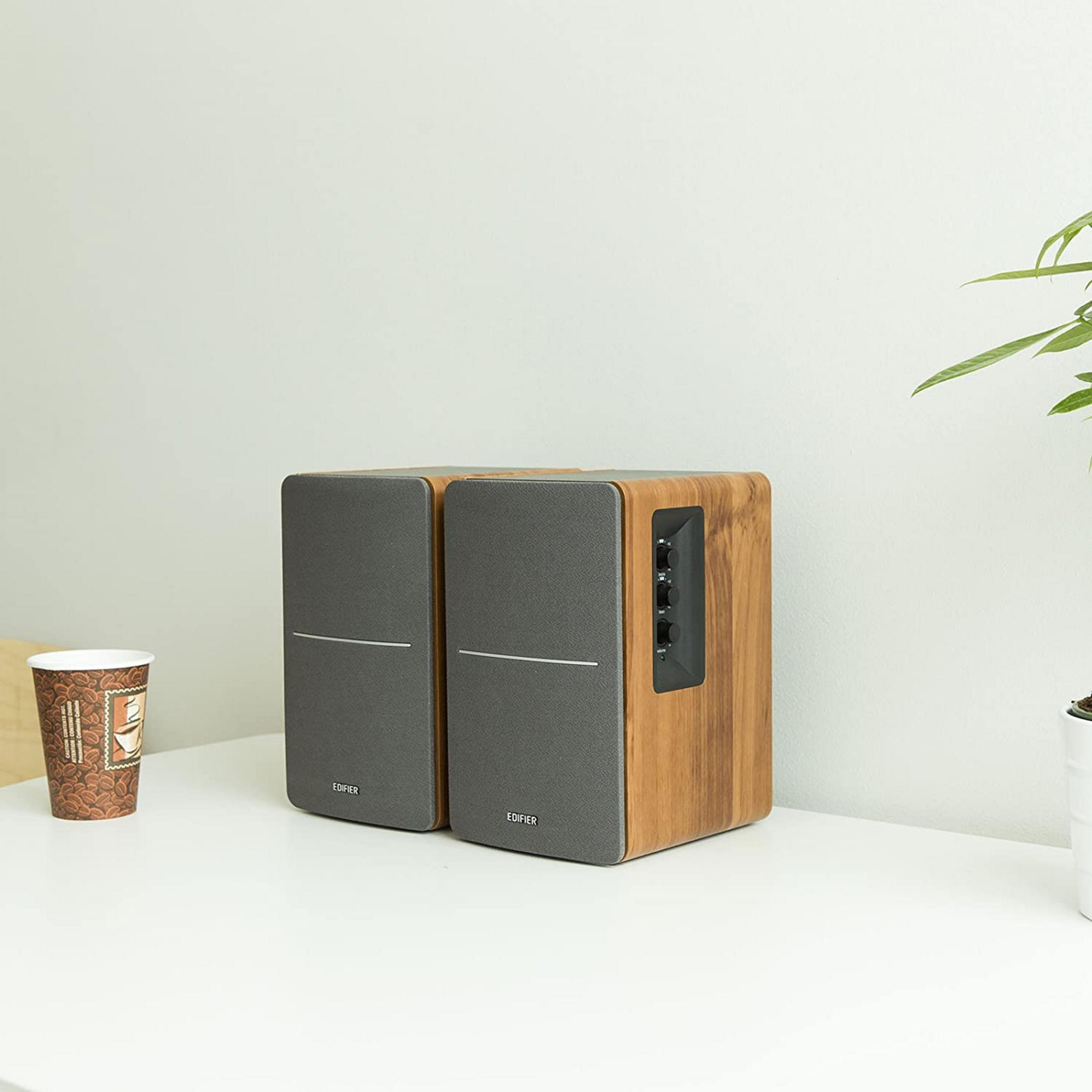 Twee grijze luidsprekers met houten accenten naast een koffiekopje op een witte tafel.