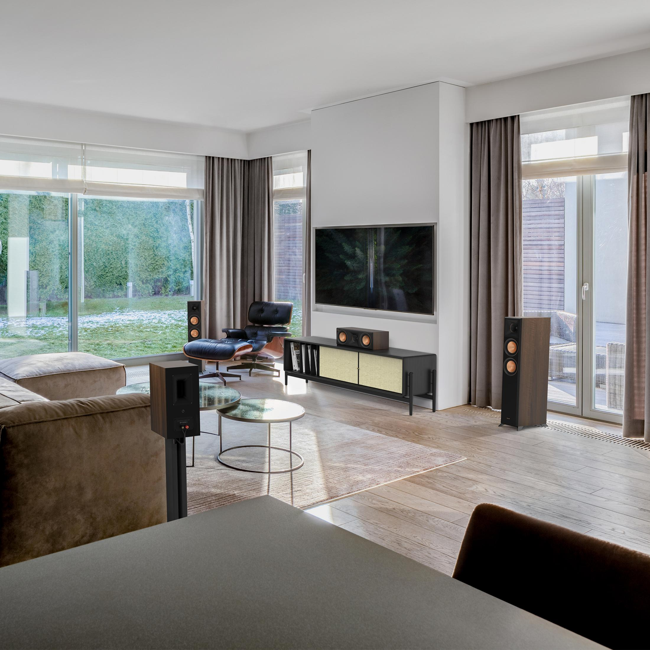 Ein modernes Wohnzimmer mit brauner Couch, schwarzem Ledersessel, TV, Lautsprechern und Glascouchtischen.