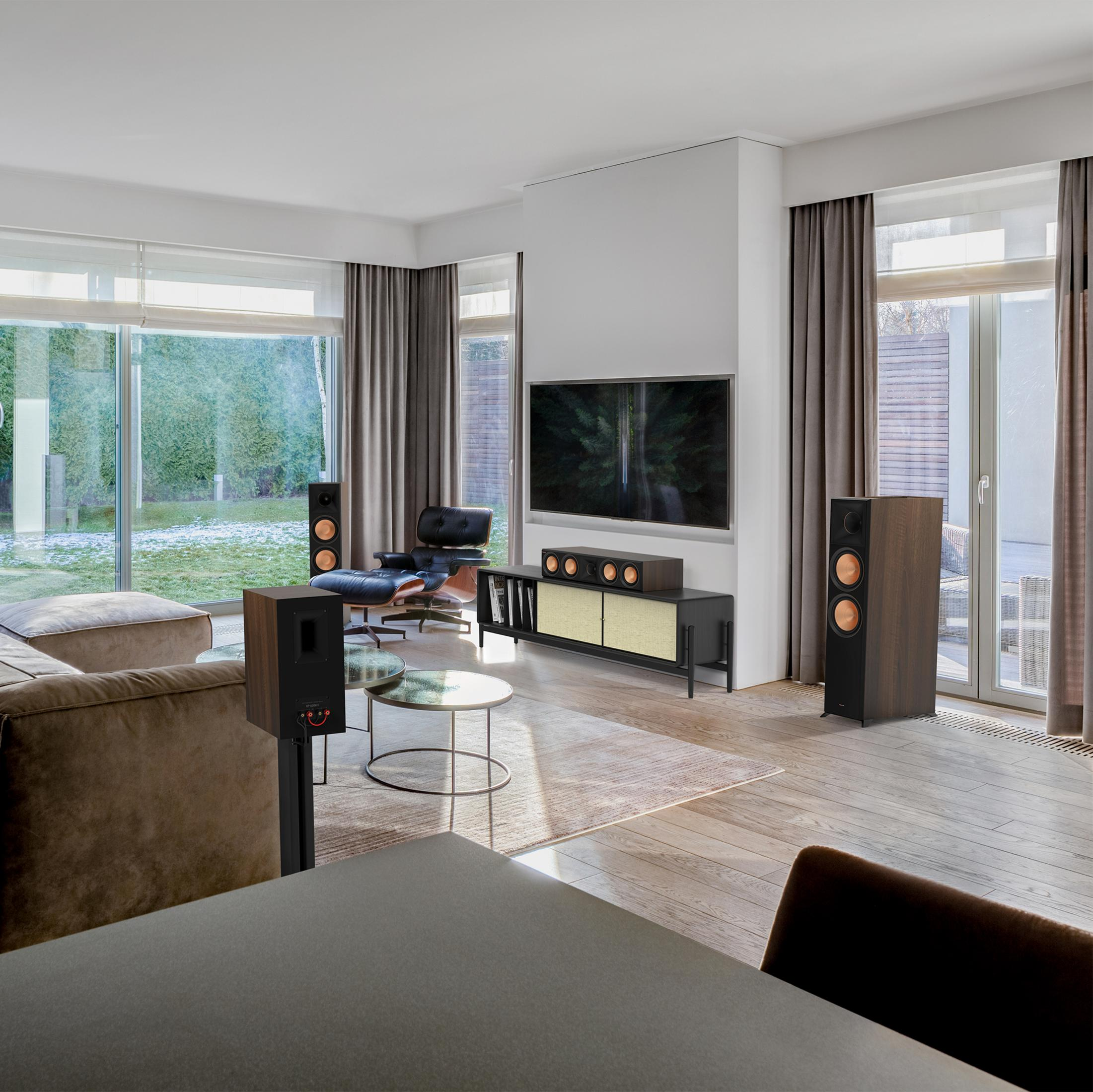 Ein modernes Wohnzimmer mit brauner Couch, Fernseher, Lautsprechern und großen Fenstern.
