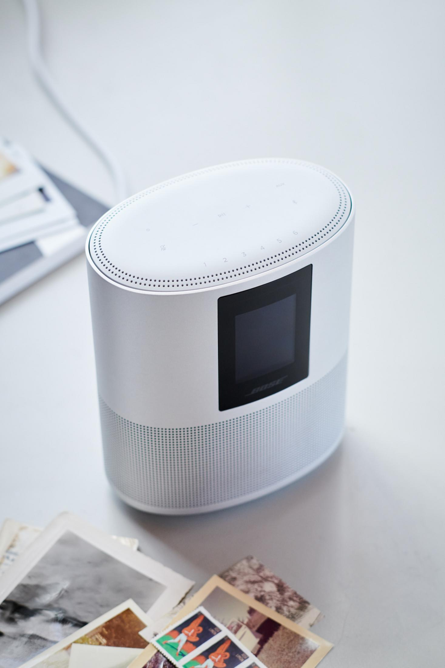Ein weißer Bose Smart Speaker mit kleinem Bildschirm steht auf einem Tisch mit alten Fotos.