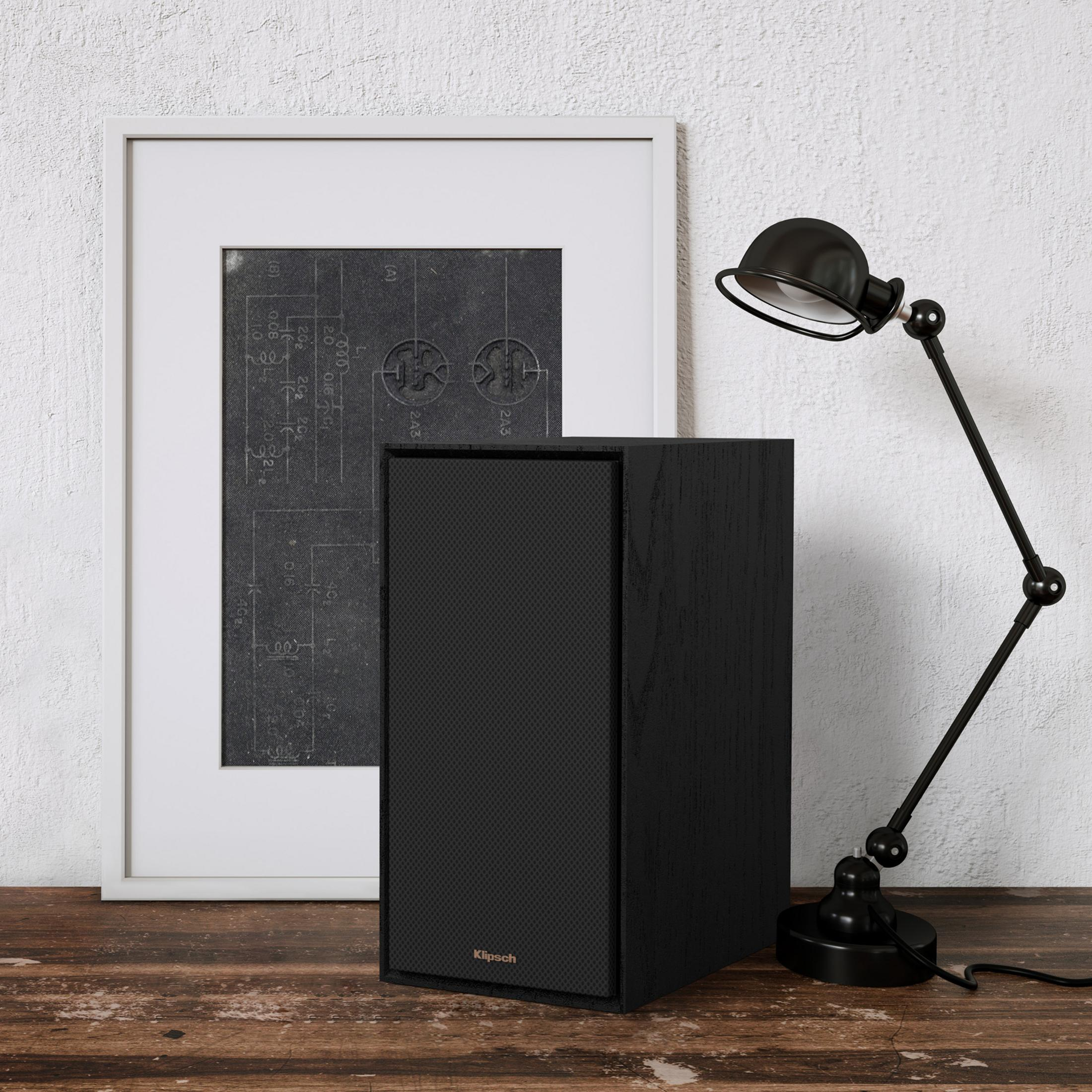 Un altoparlante nero siede accanto a un diagramma tecnico incorniciato e una lampada.