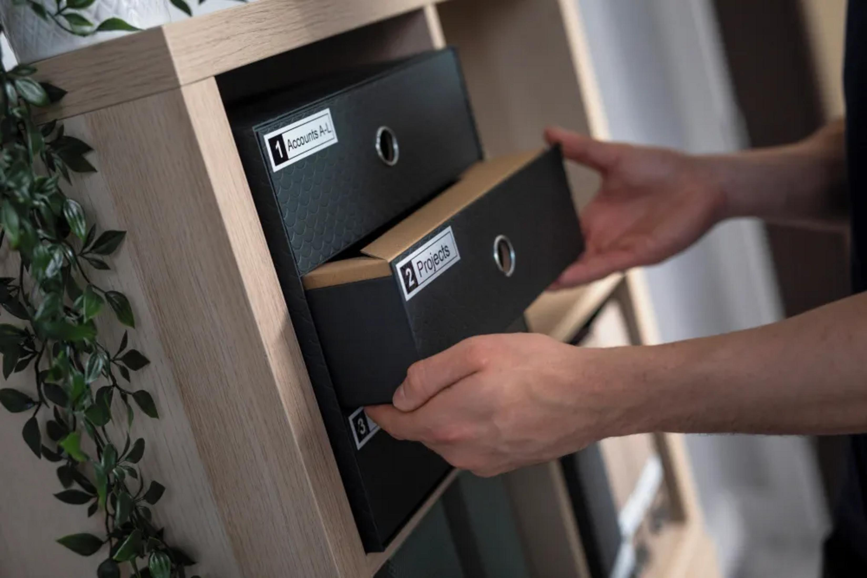 Osoba sortująca foldery w regale. Wyciągany jest folder z napisem "Projekty".