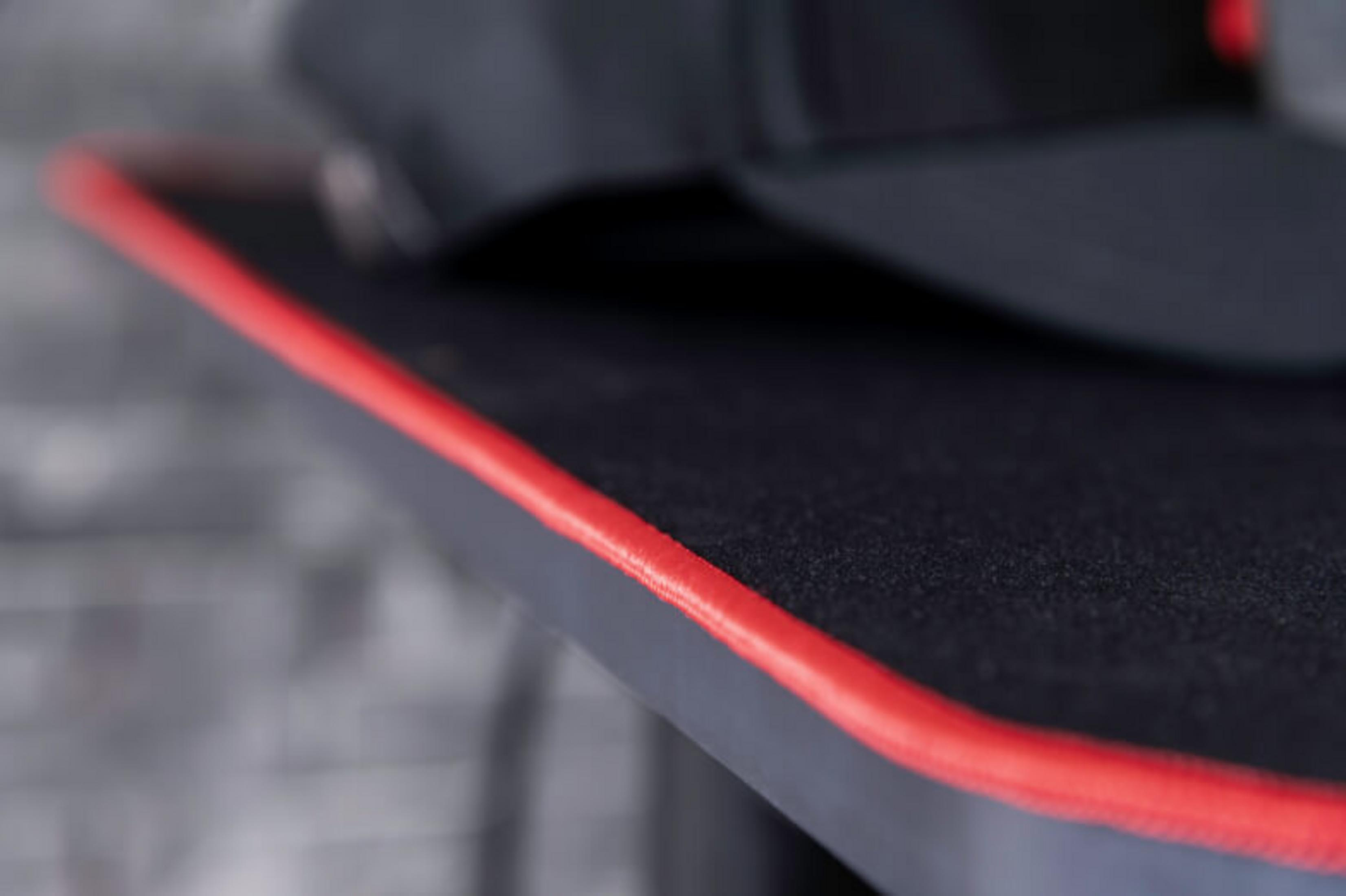 Un berretto da baseball nero con cuciture rosse su una superficie grigia.
