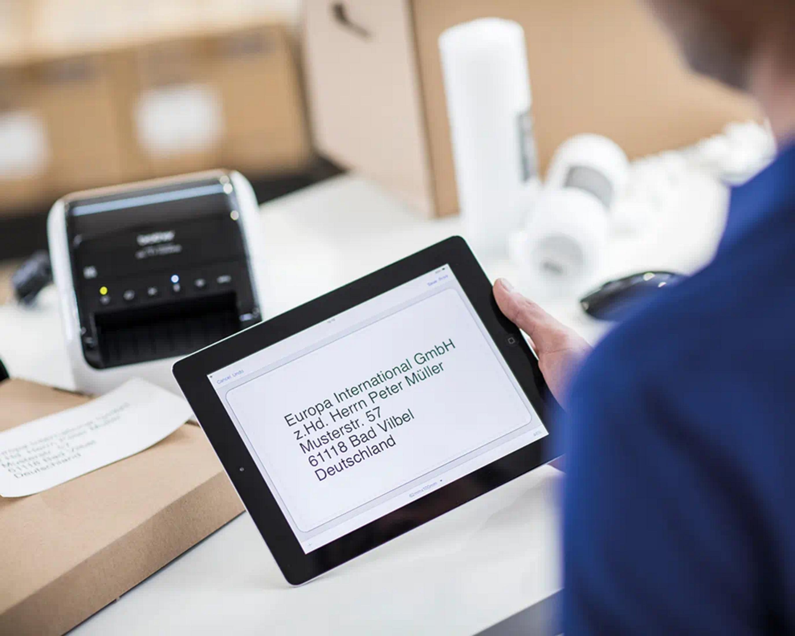 A tablet displays an address, next to a printer and packages.
