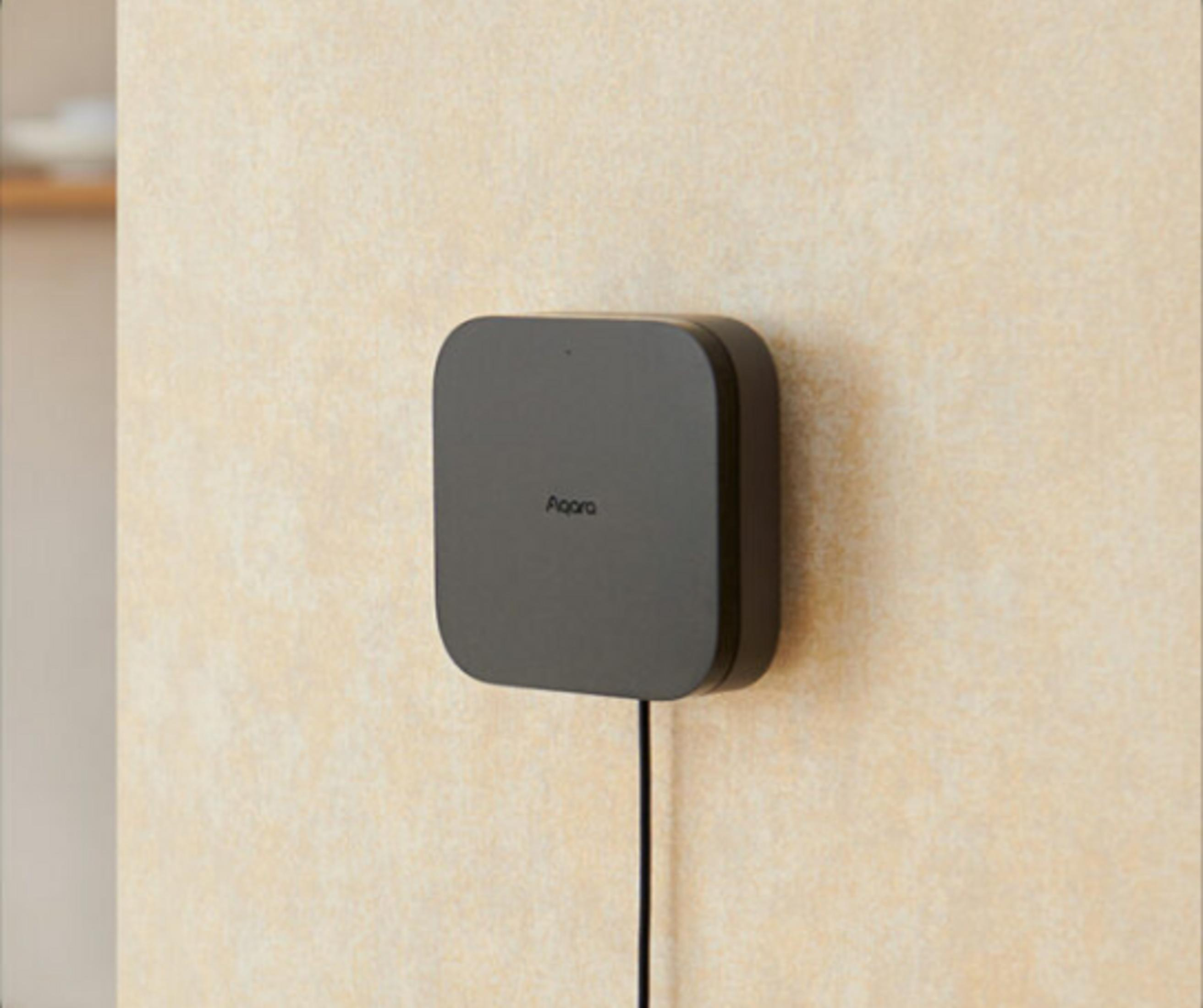 Ein dunkler, quadratischer Sensor mit abgerundeten Ecken hängt an einer cremefarbenen Wand.