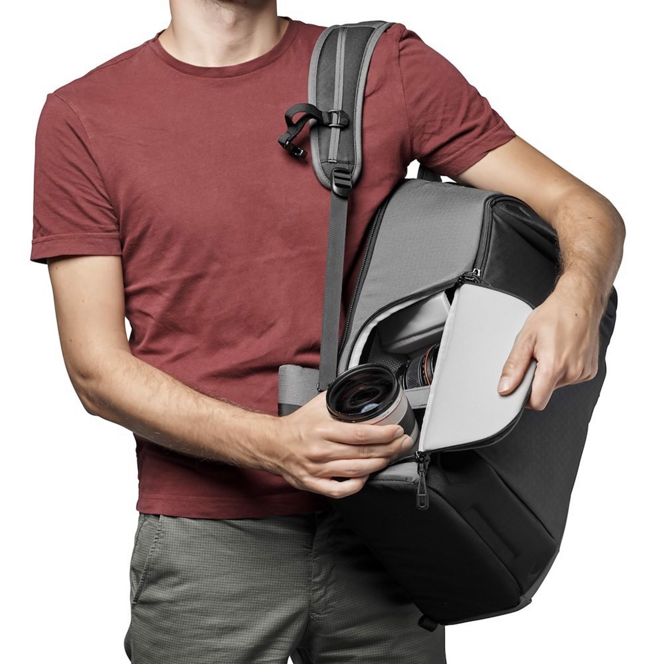 Homme en chemise rouge rangeant un objectif dans un sac photo gris.