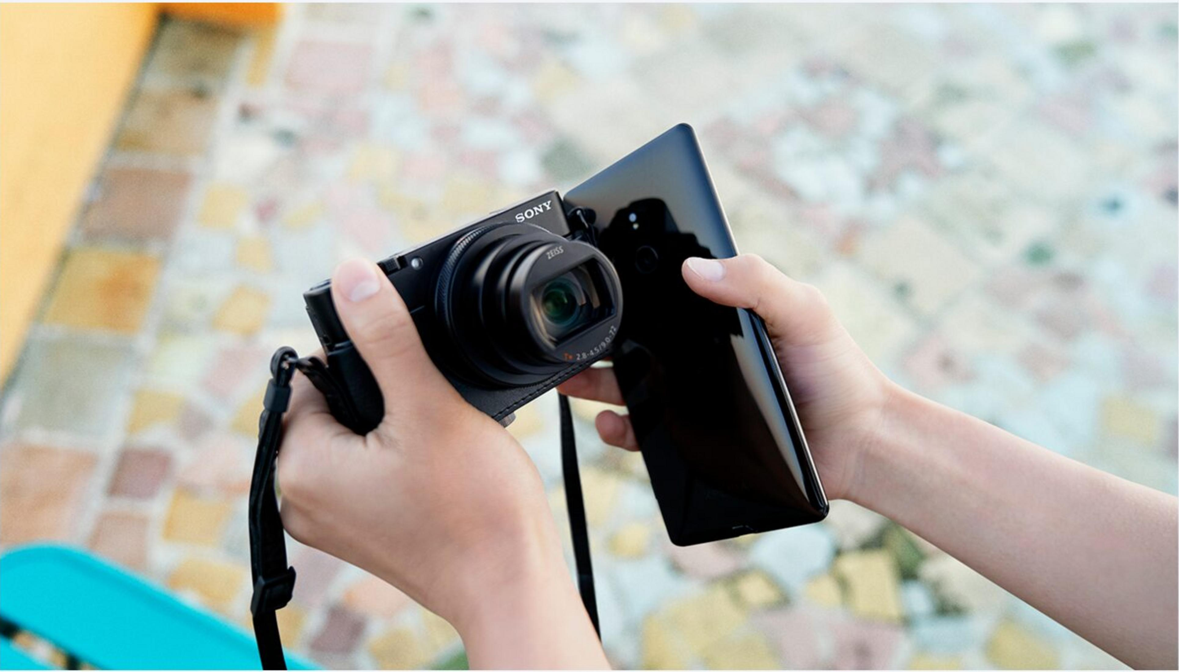 Manos sostienen una cámara Sony negra y un smartphone negro.