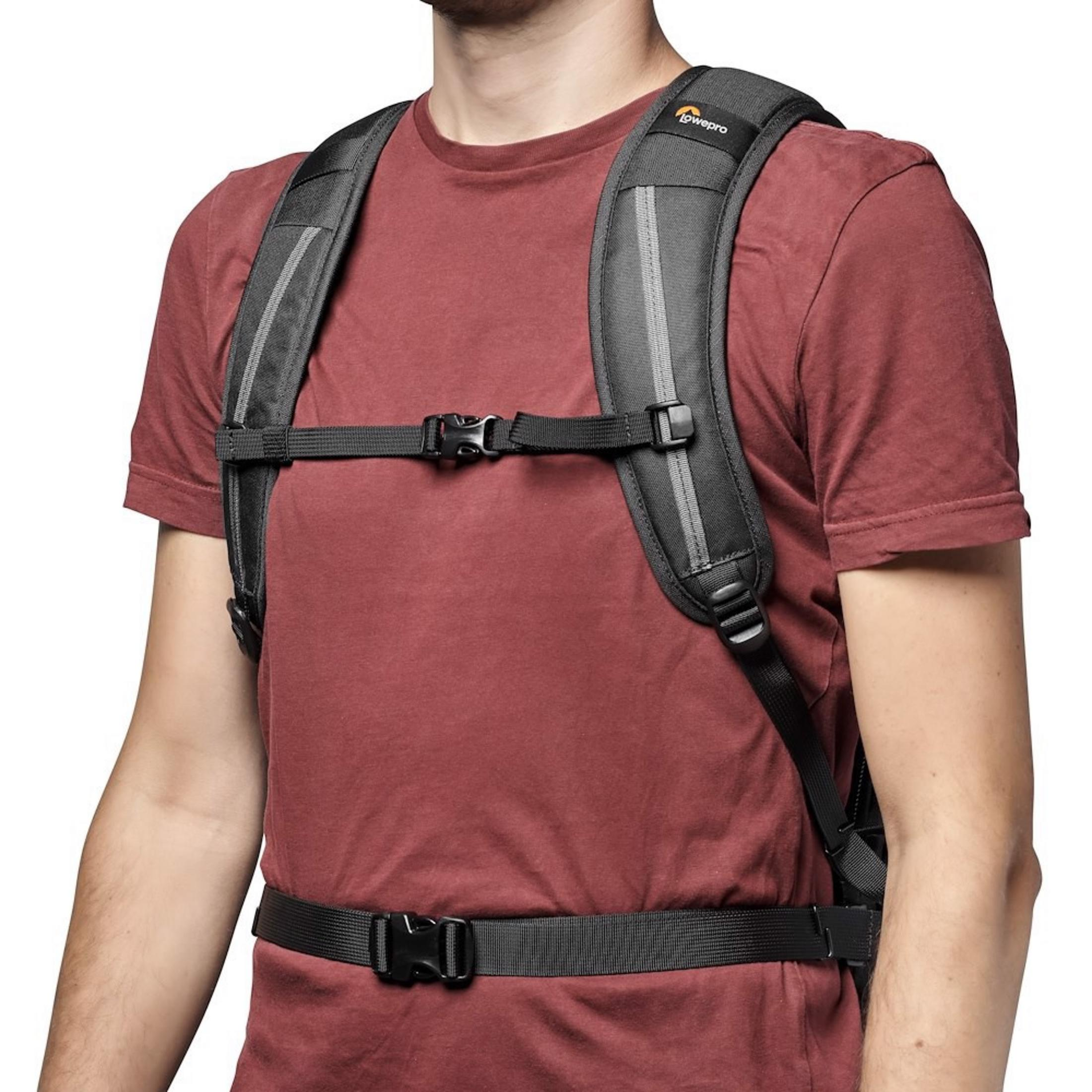 Een man in een rood T-shirt draagt een zwarte rugzak met borst- en heupbanden.