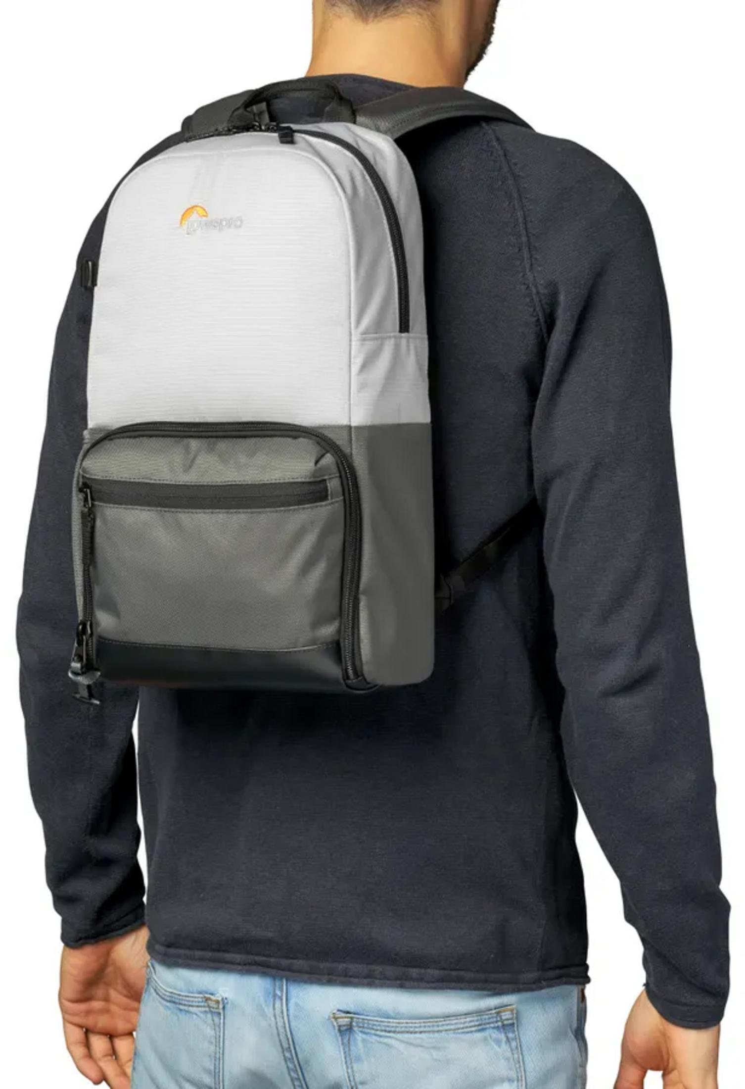 Un homme porte un sac à dos gris et blanc avec logo Lowepro. Il porte un t-shirt noir à manches longues et un jean.