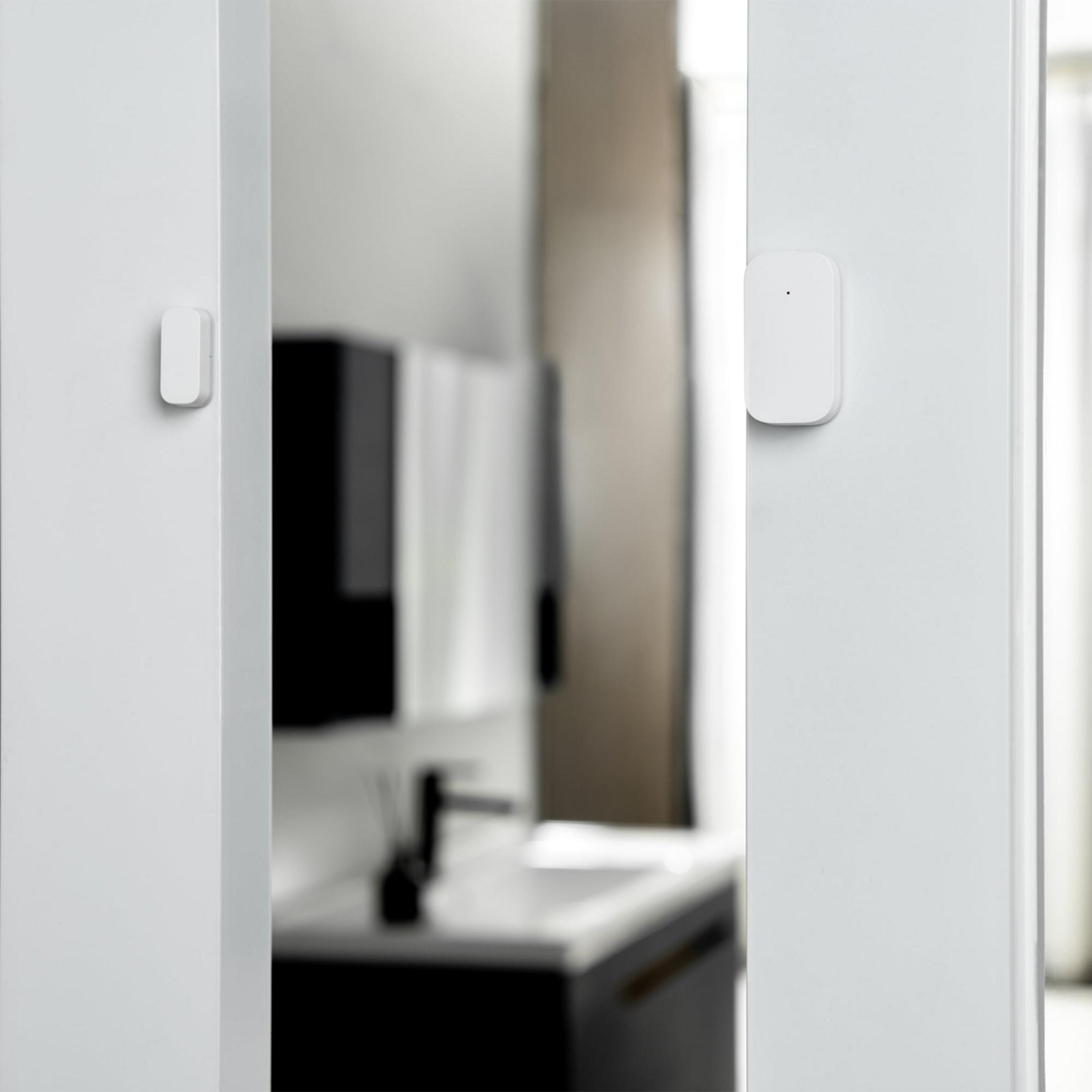 Un sensore bianco su una porta bianca con un bagno sullo sfondo.
