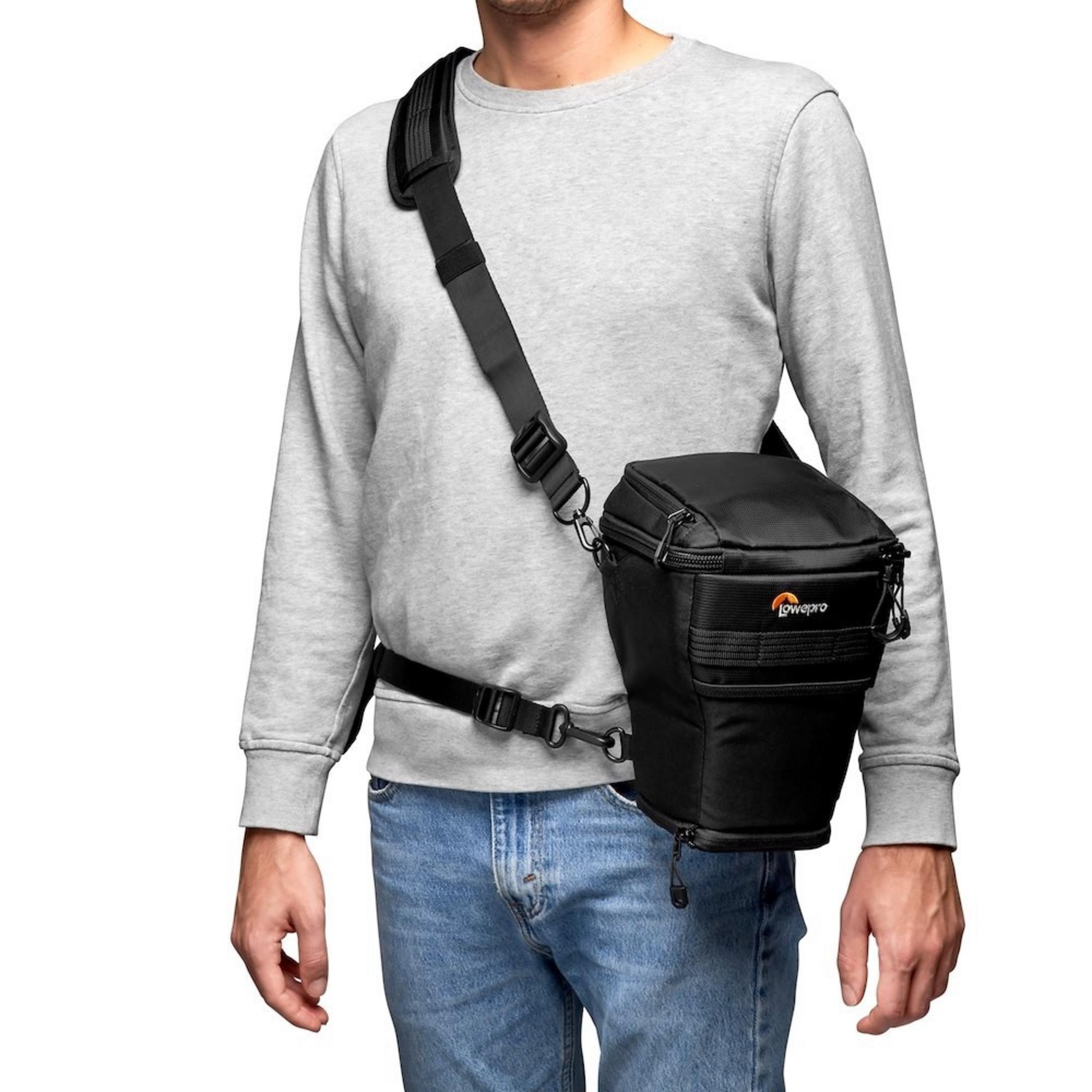 Mann trägt eine graue Sweatjacke, blaue Jeans und eine schwarze Kameratasche über der Schulter.