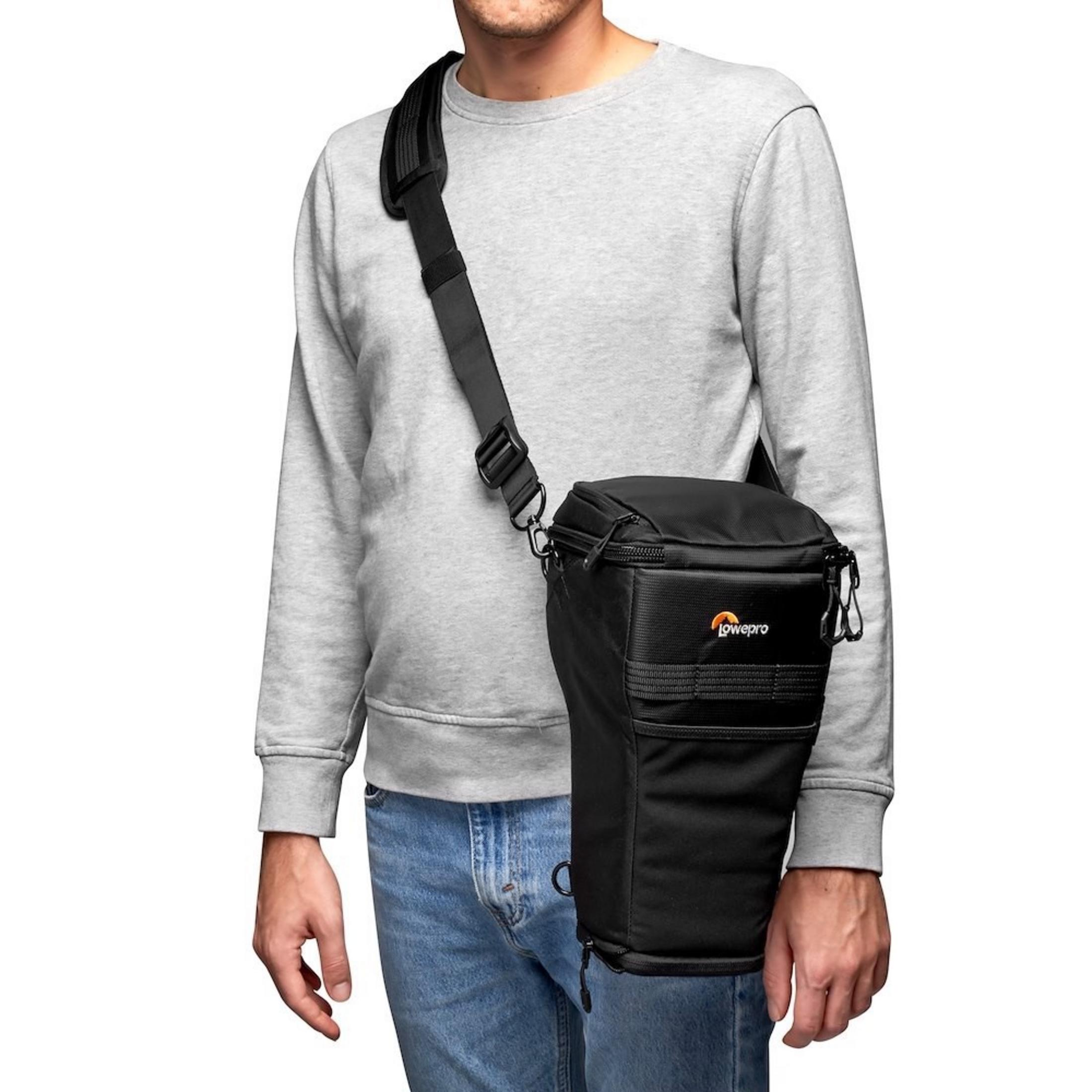 Un uomo indossa felpa grigia e jeans blu, con borsa fotografica Lowepro nera a tracolla.