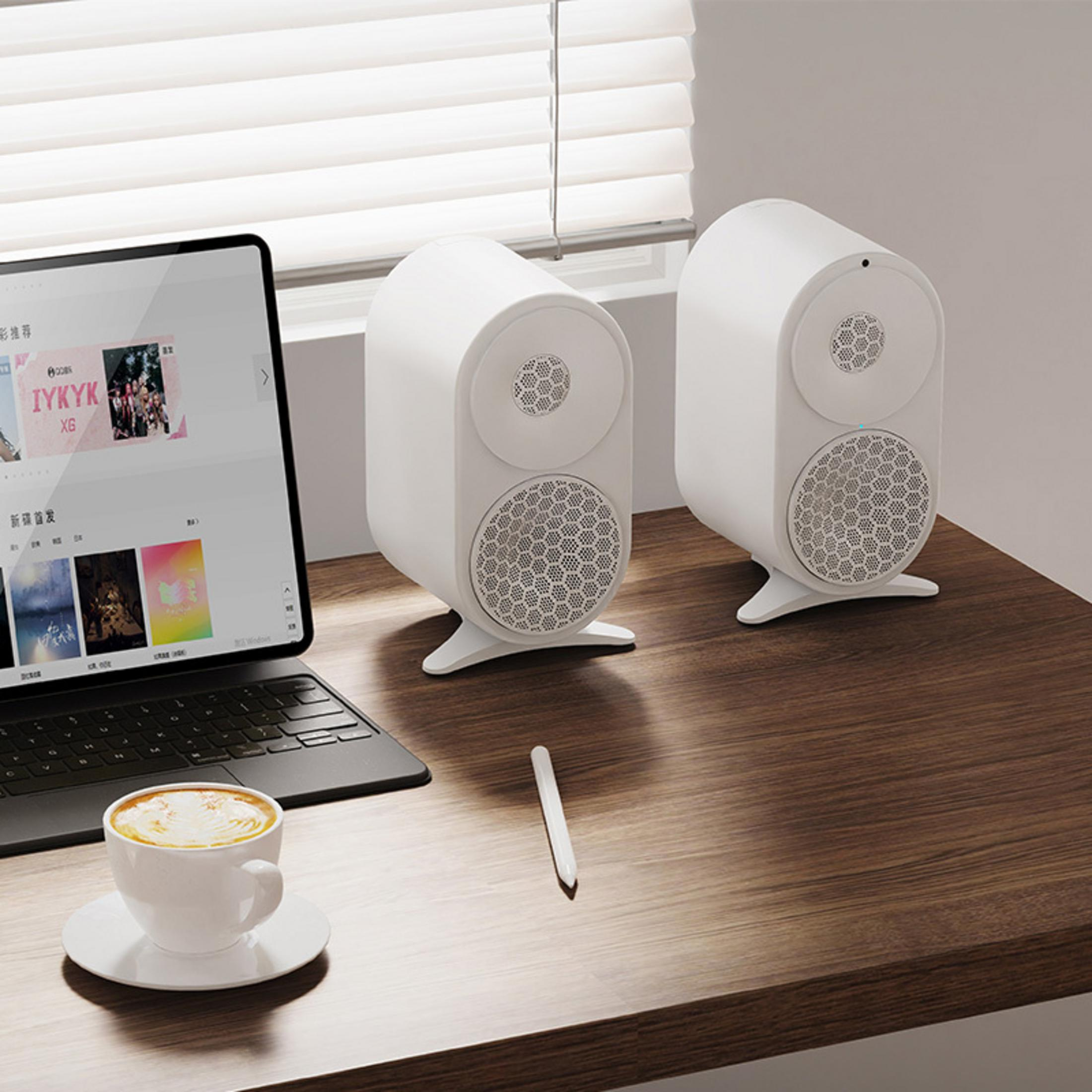 Dos altavoces blancos sobre un escritorio de madera junto a un portátil y una taza de café.