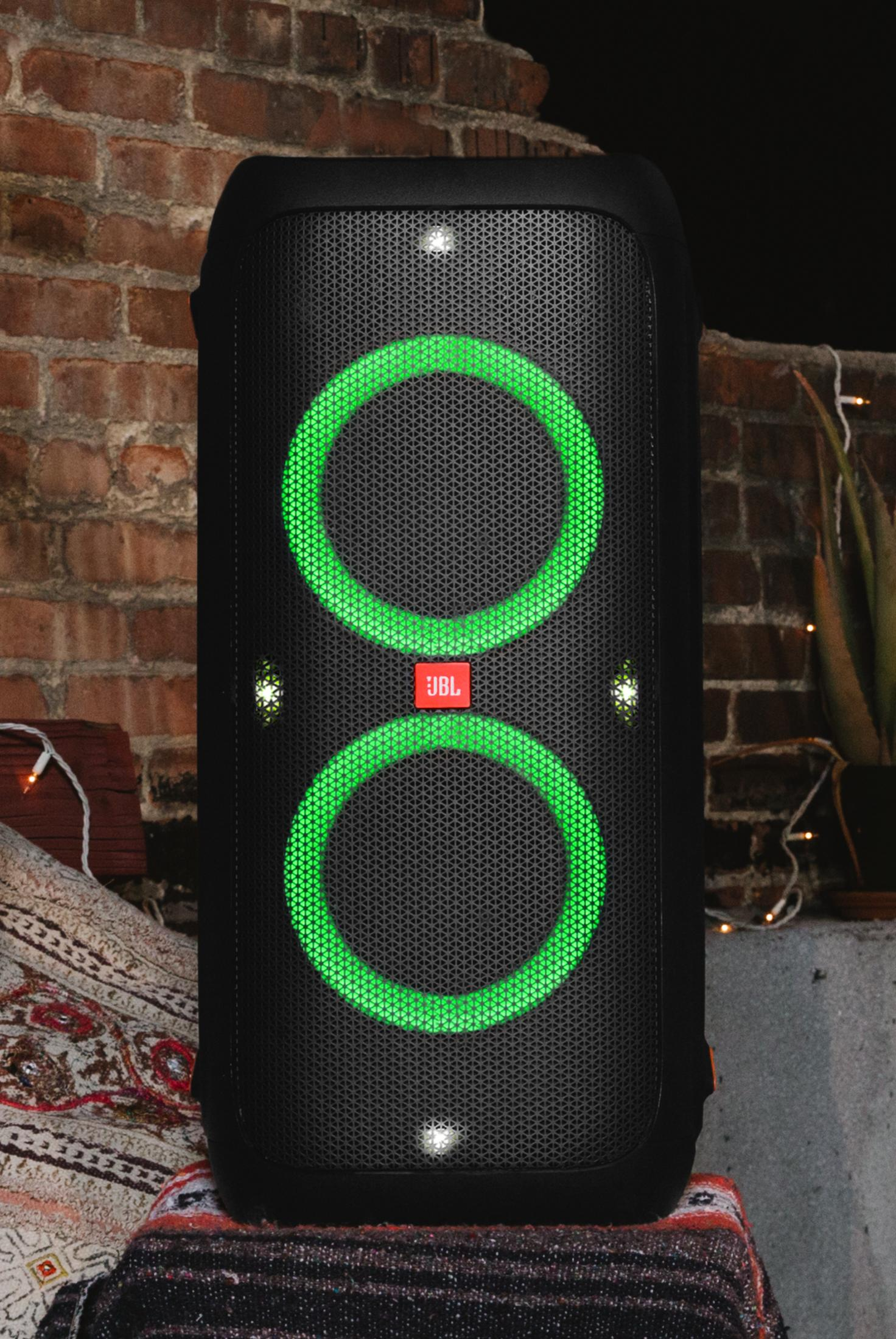 Un altoparlante JBL nero con due anelli luminosi verdi davanti a un muro di mattoni.