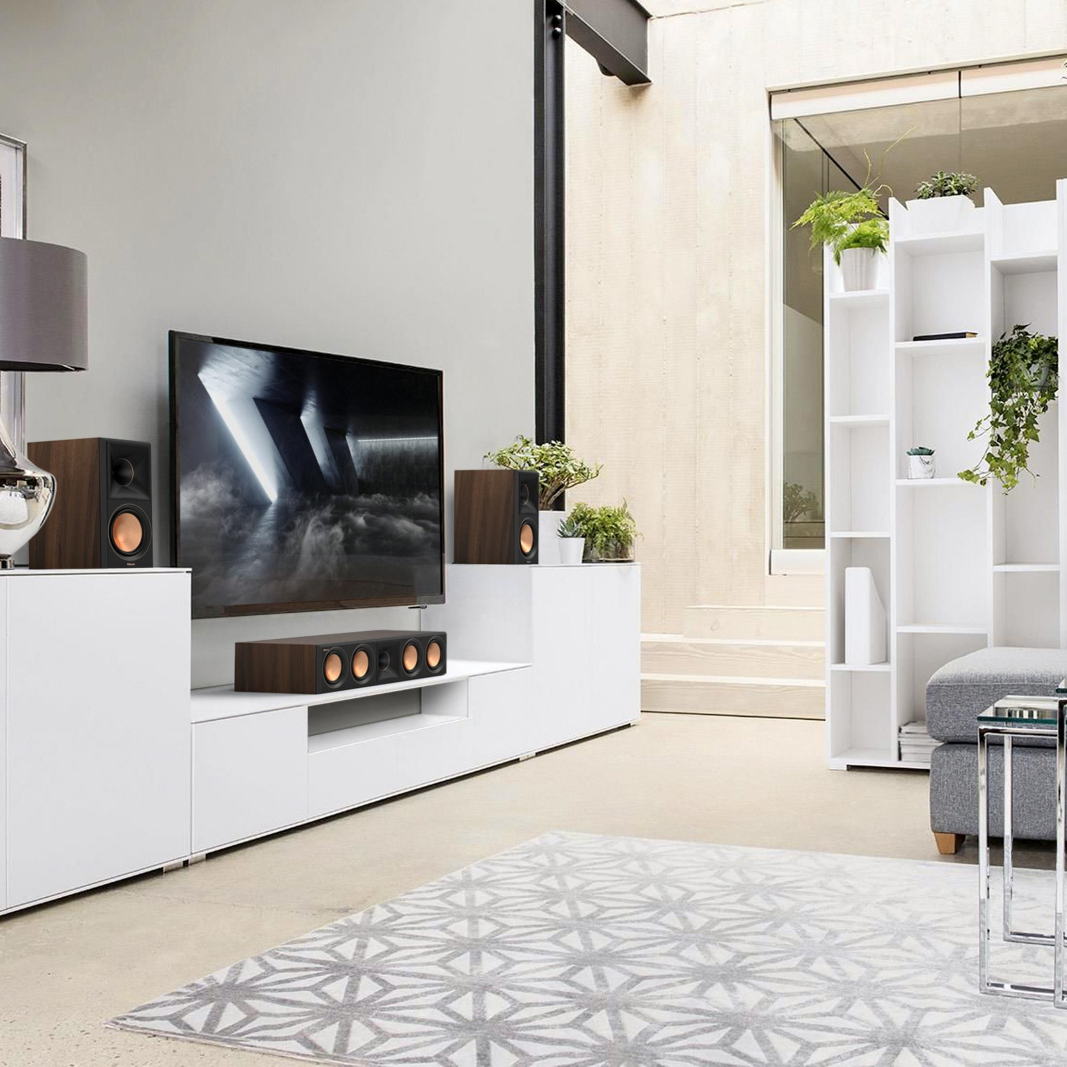 Modernes Wohnzimmer mit weißen Möbeln, Lautsprechern, TV, Pflanzen und gemustertem Teppich.