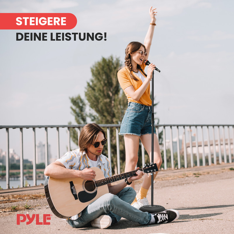 Mann spielt Gitarre, Frau singt ins Mikrofon, beide im Freien.