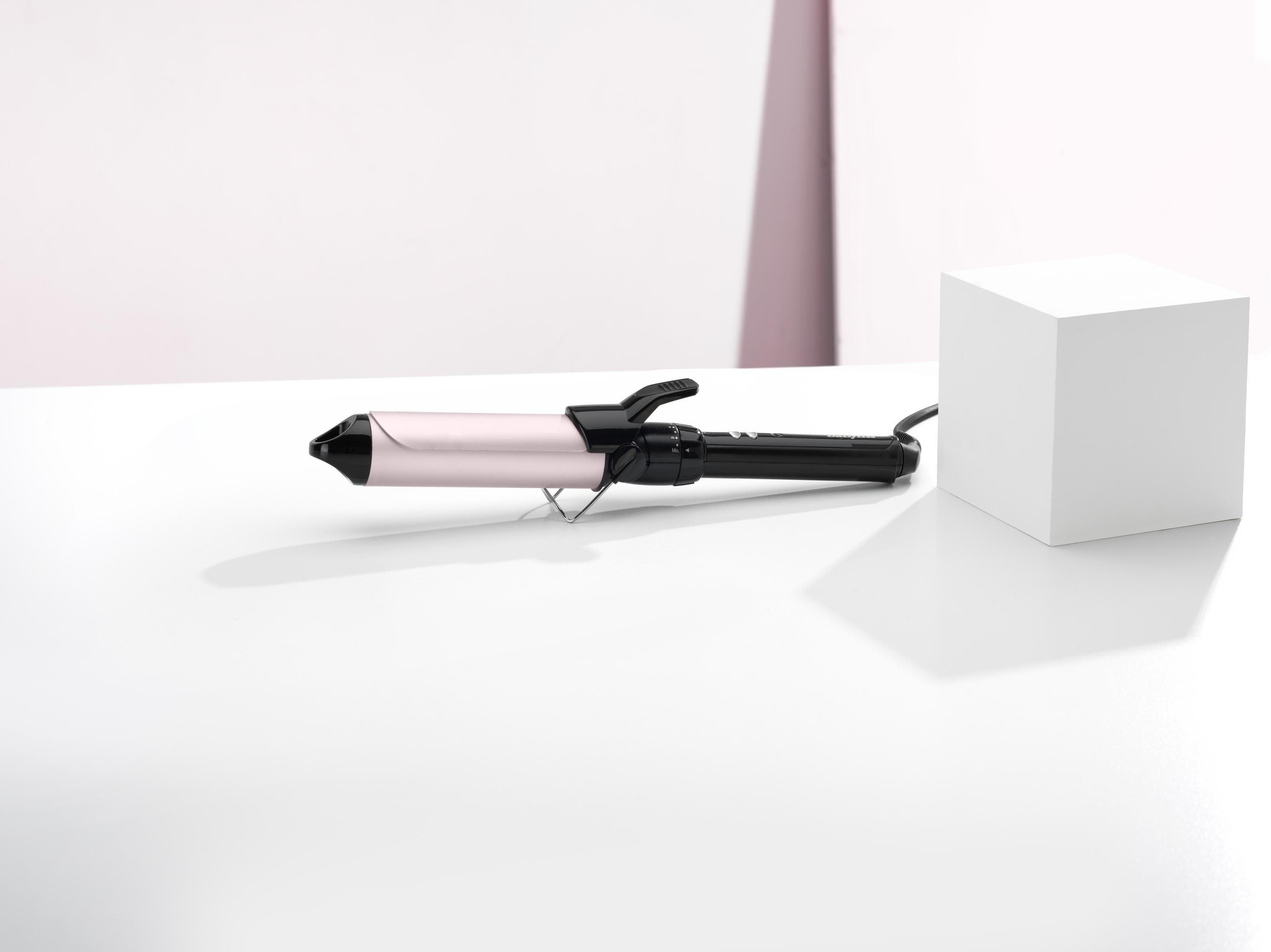 Un arricciacapelli color oro rosa con manico e supporto neri su superficie bianca.