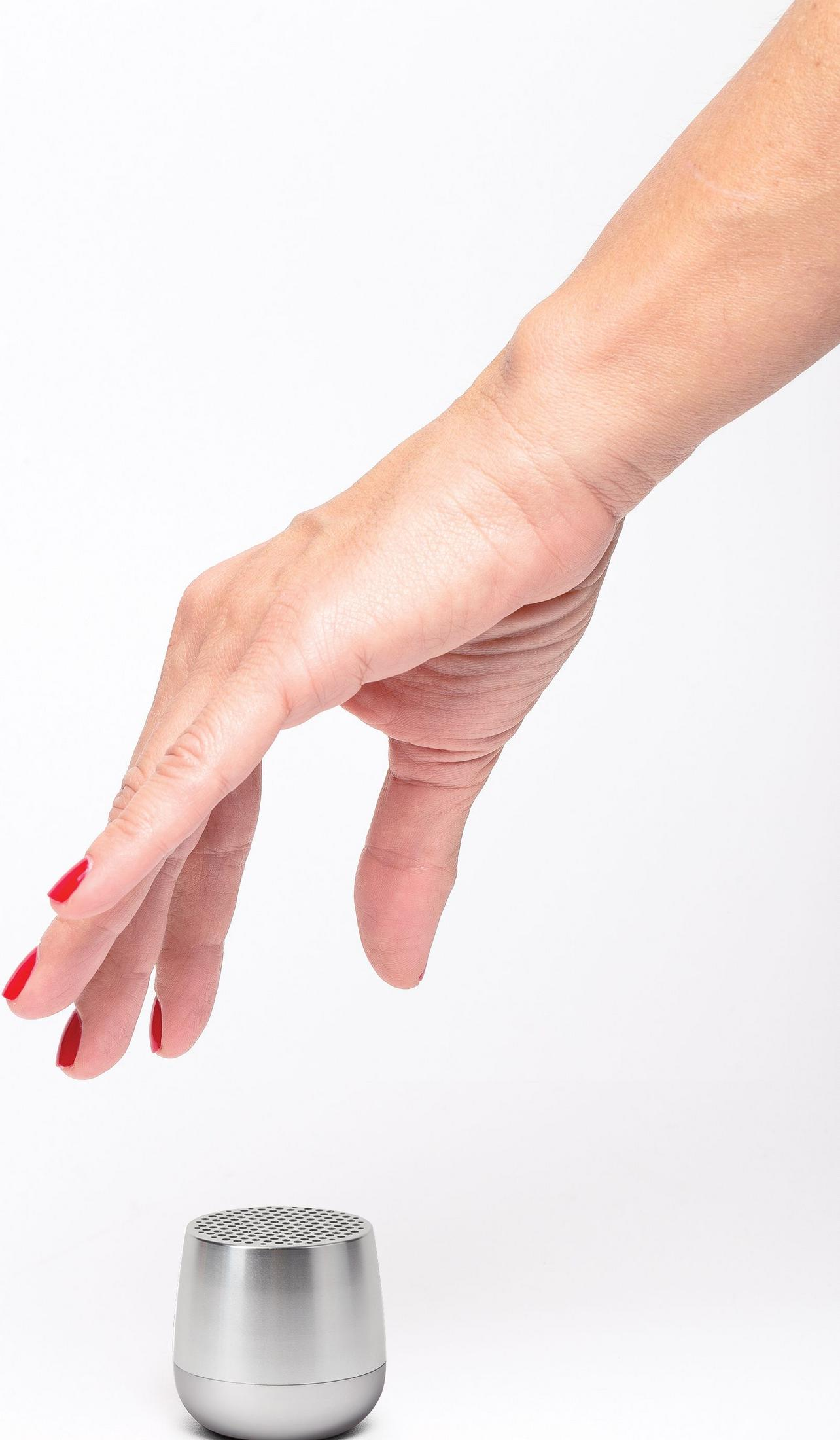 Eine Hand mit roten Nägeln nähert sich einem kleinen silbernen Lautsprecher.
