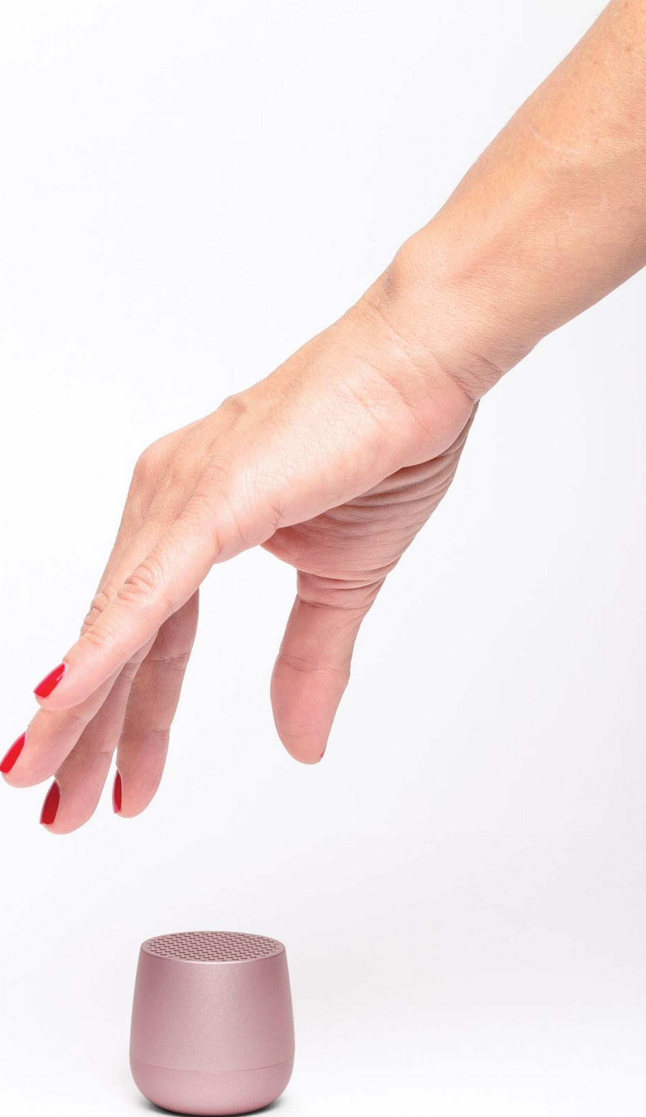 Eine Hand mit roten Nägeln greift nach einem kleinen rosafarbenen Lautsprecher.