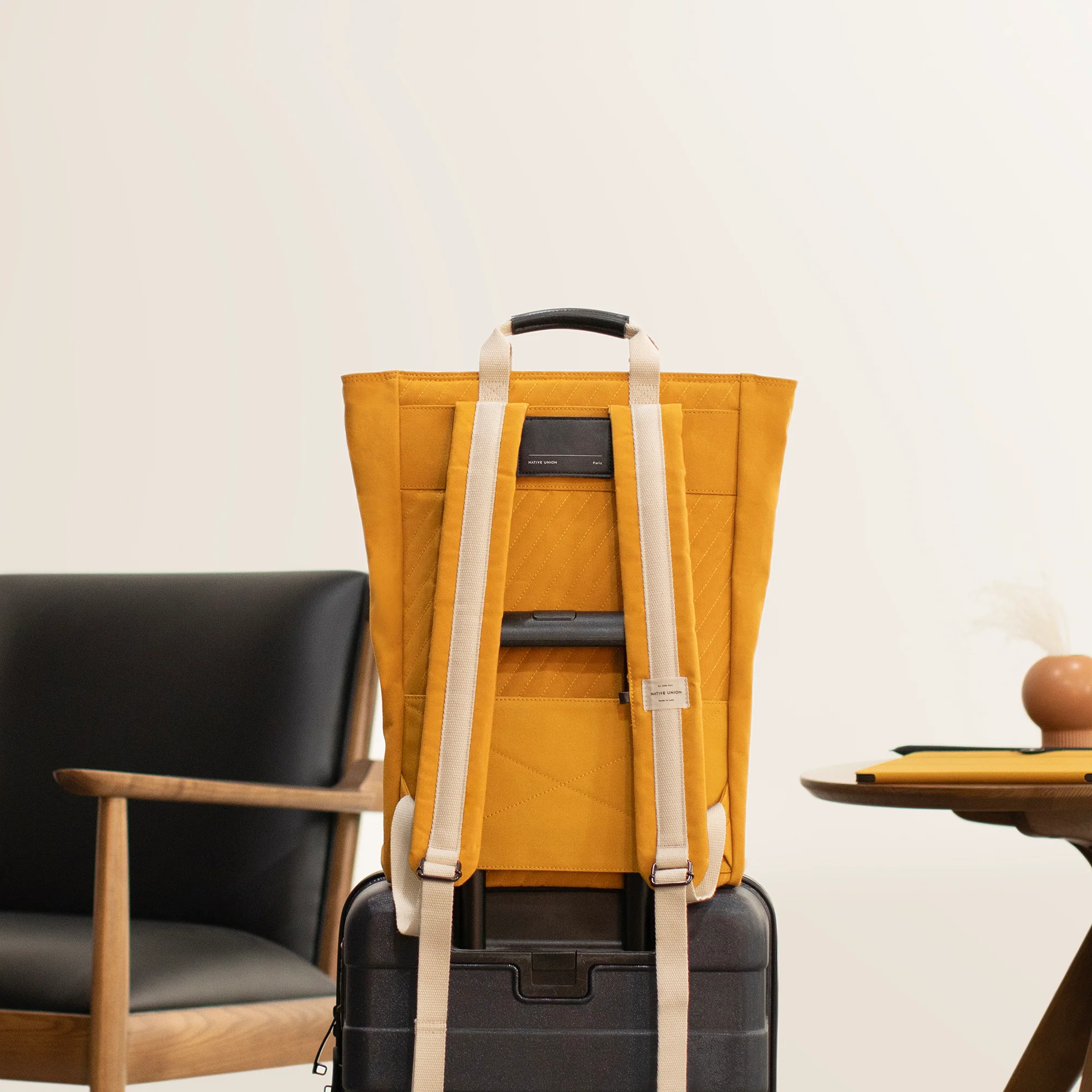 Gelber Rucksack auf schwarzem Koffer, daneben ein Stuhl und ein Tisch.