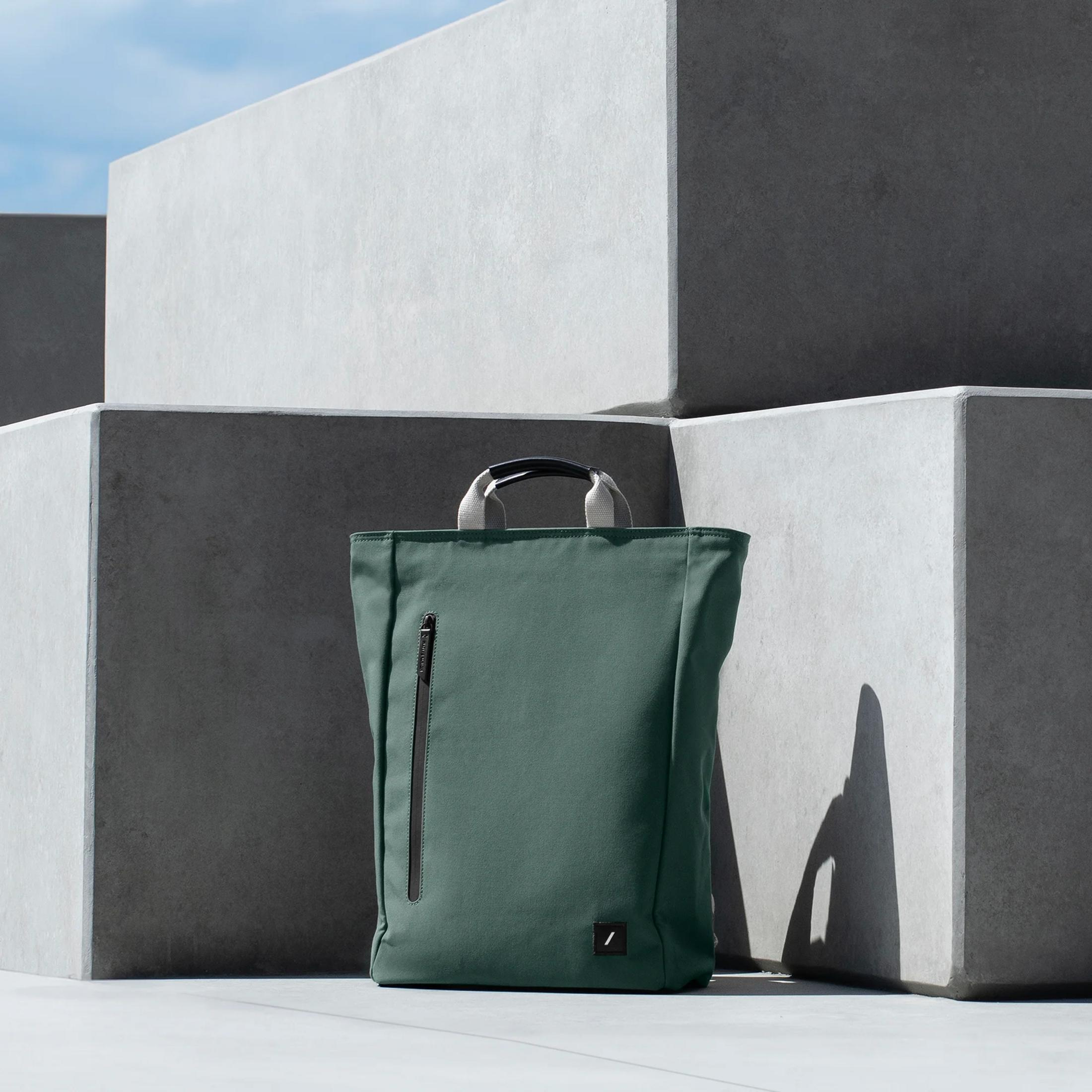 Ein dunkelgrüner Rucksack steht vor grauen Betonwürfeln unter blauem Himmel.