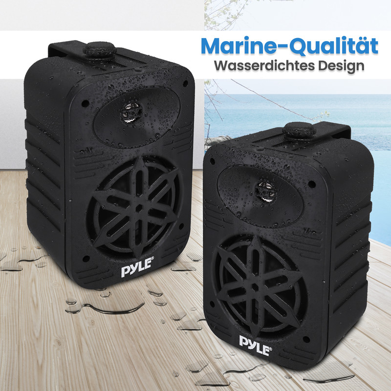 Zwei schwarze wasserdichte Lautsprecher auf Holz mit Wasserflecken, Meer im Hintergrund.