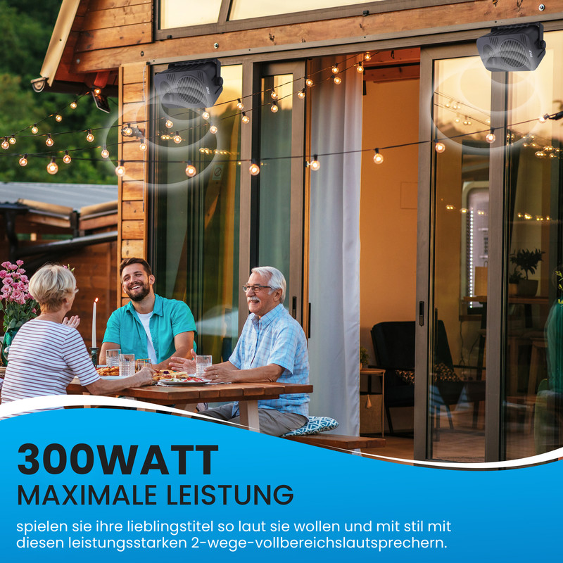 Drei Personen sitzen an einem Tisch im Freien, zwei Lautsprecher sind montiert.