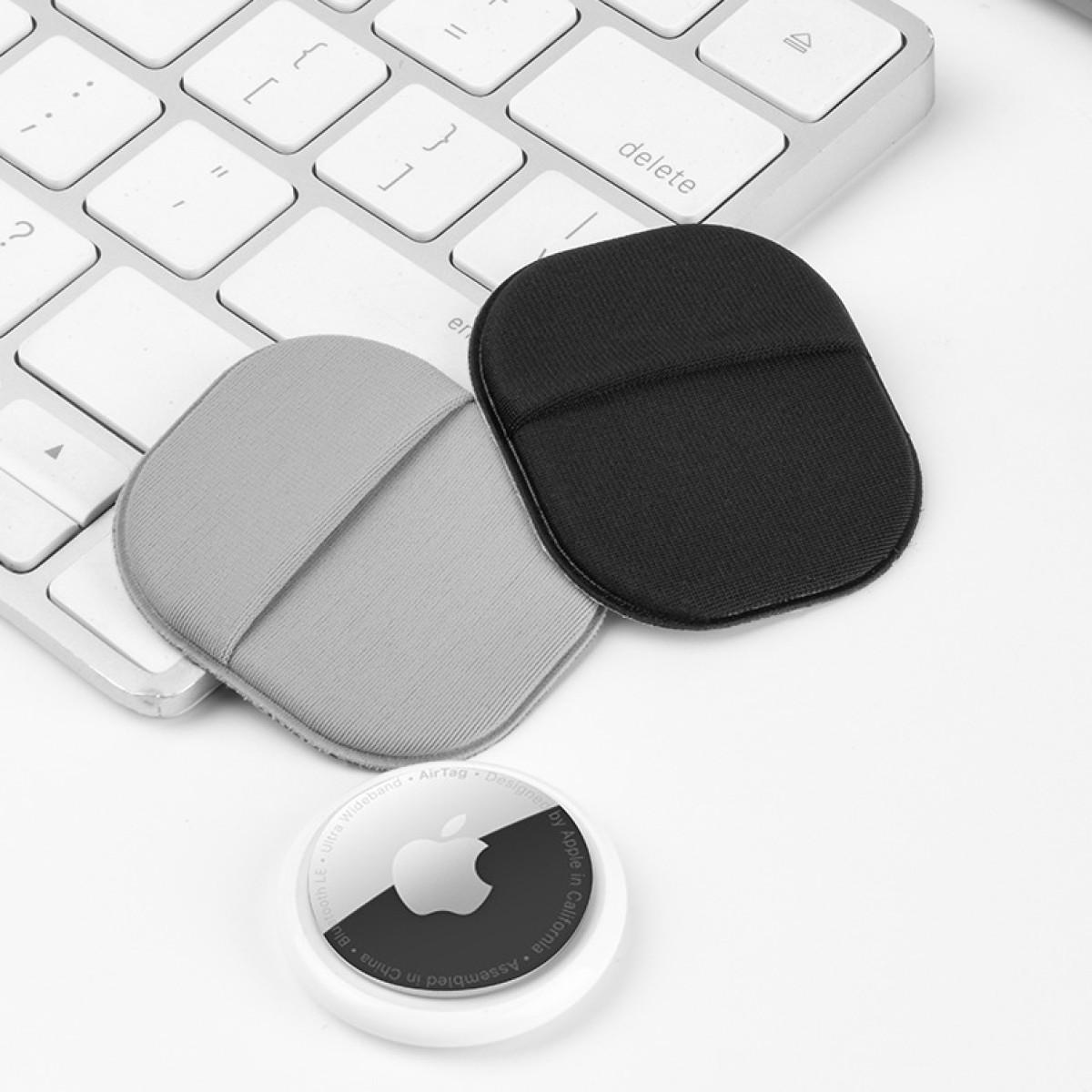 Zwei gepolsterte Pads, schwarz und grau, auf einer Tastatur mit einem AirTag.