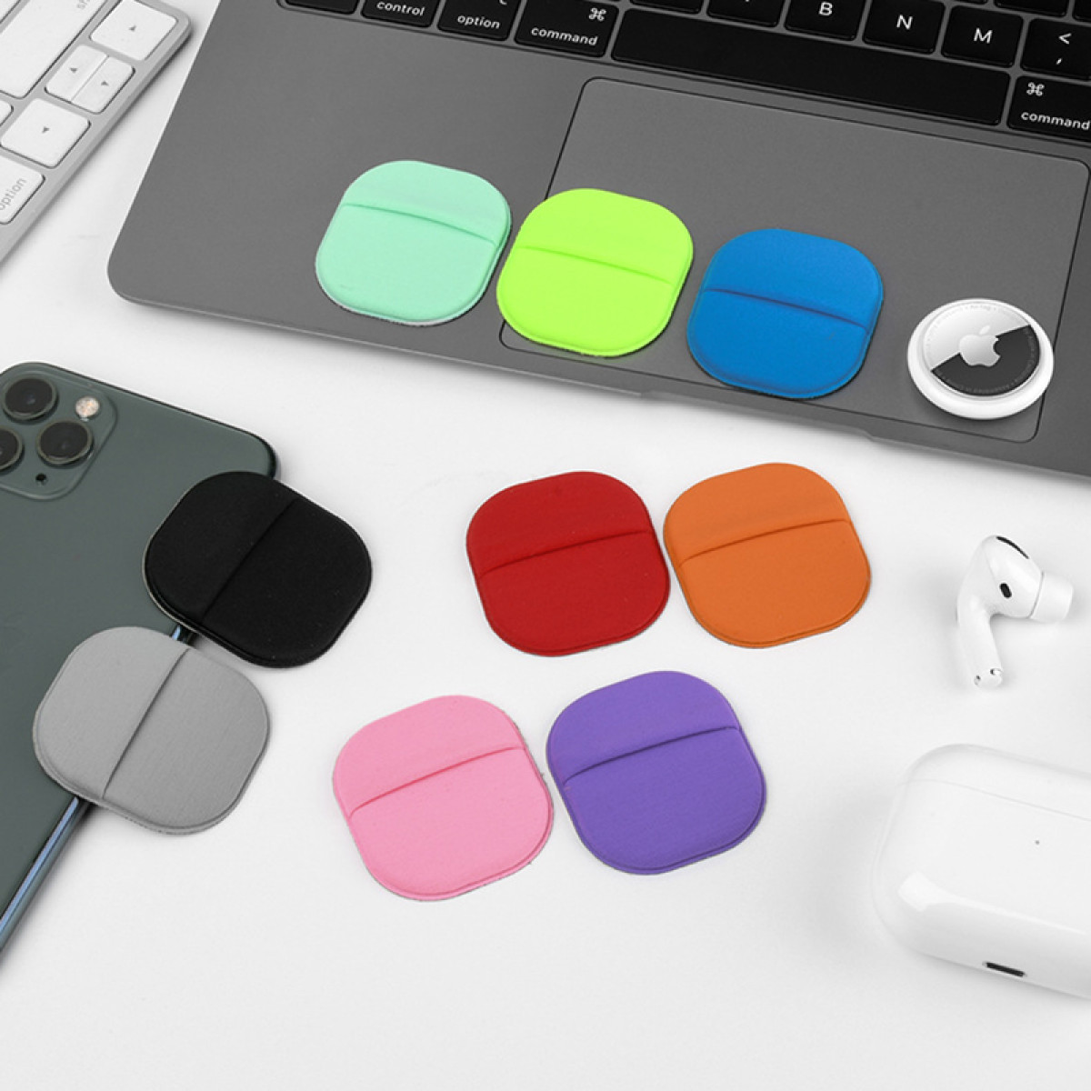 Bunte Silikonhüllen auf Laptop, Handy und Schreibtisch. Rot, Orange, Pink, Lila, Grau, Schwarz, Mint, Limettengrün und Blau.