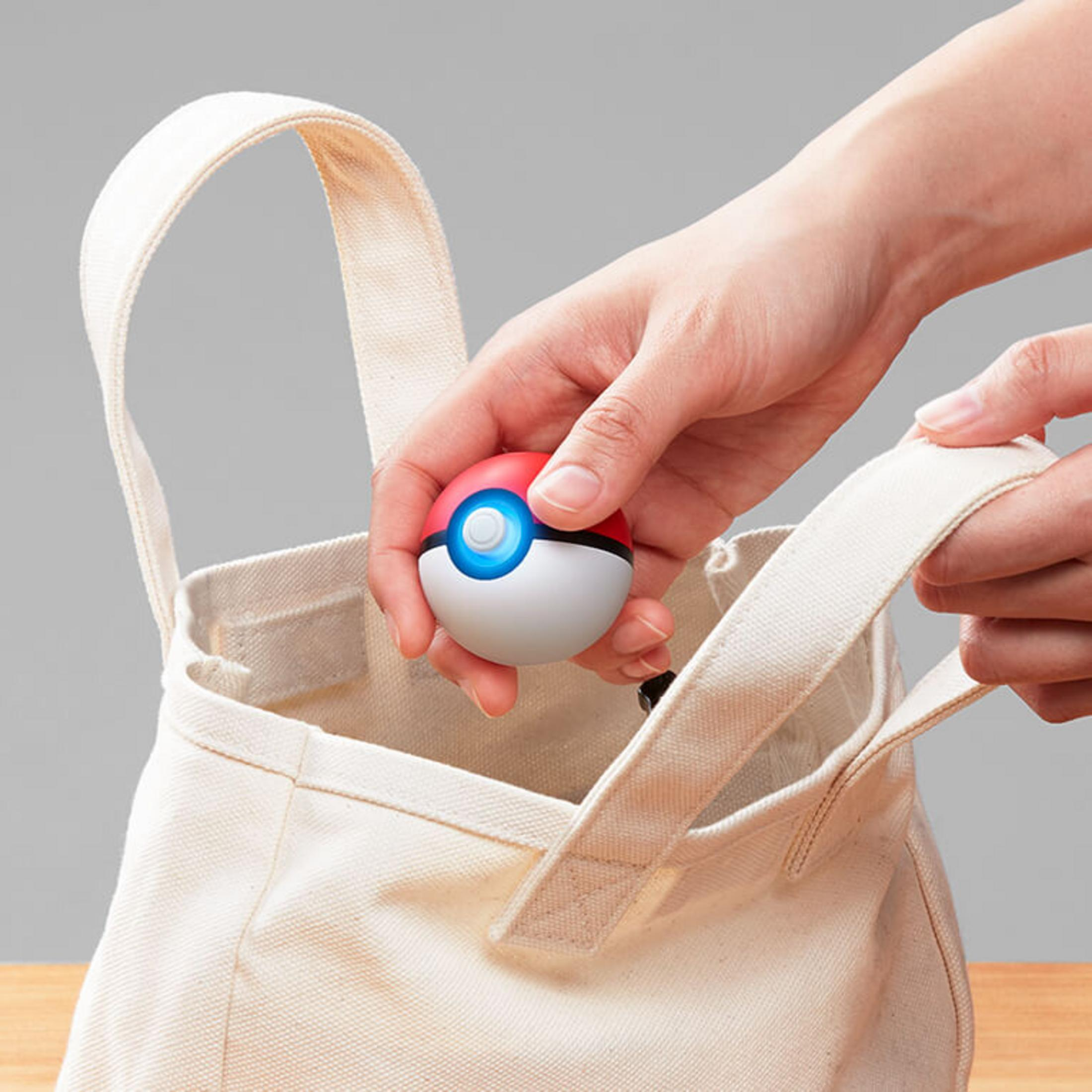 Eine Hand legt einen leuchtenden Pokeball in eine weiße Stofftasche.
