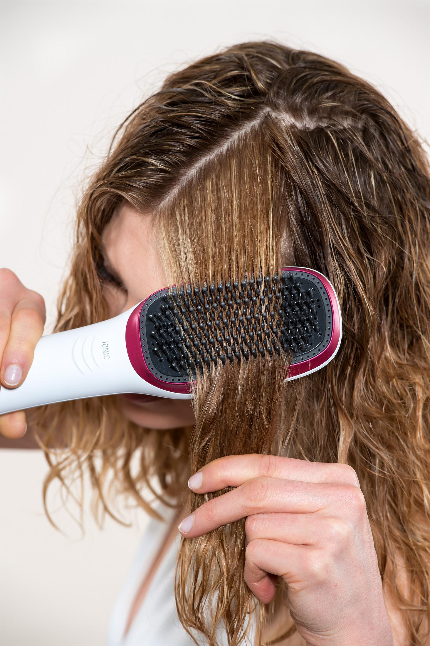 Una mujer se peina el pelo mojado y castaño con un cepillo blanco y rojo.