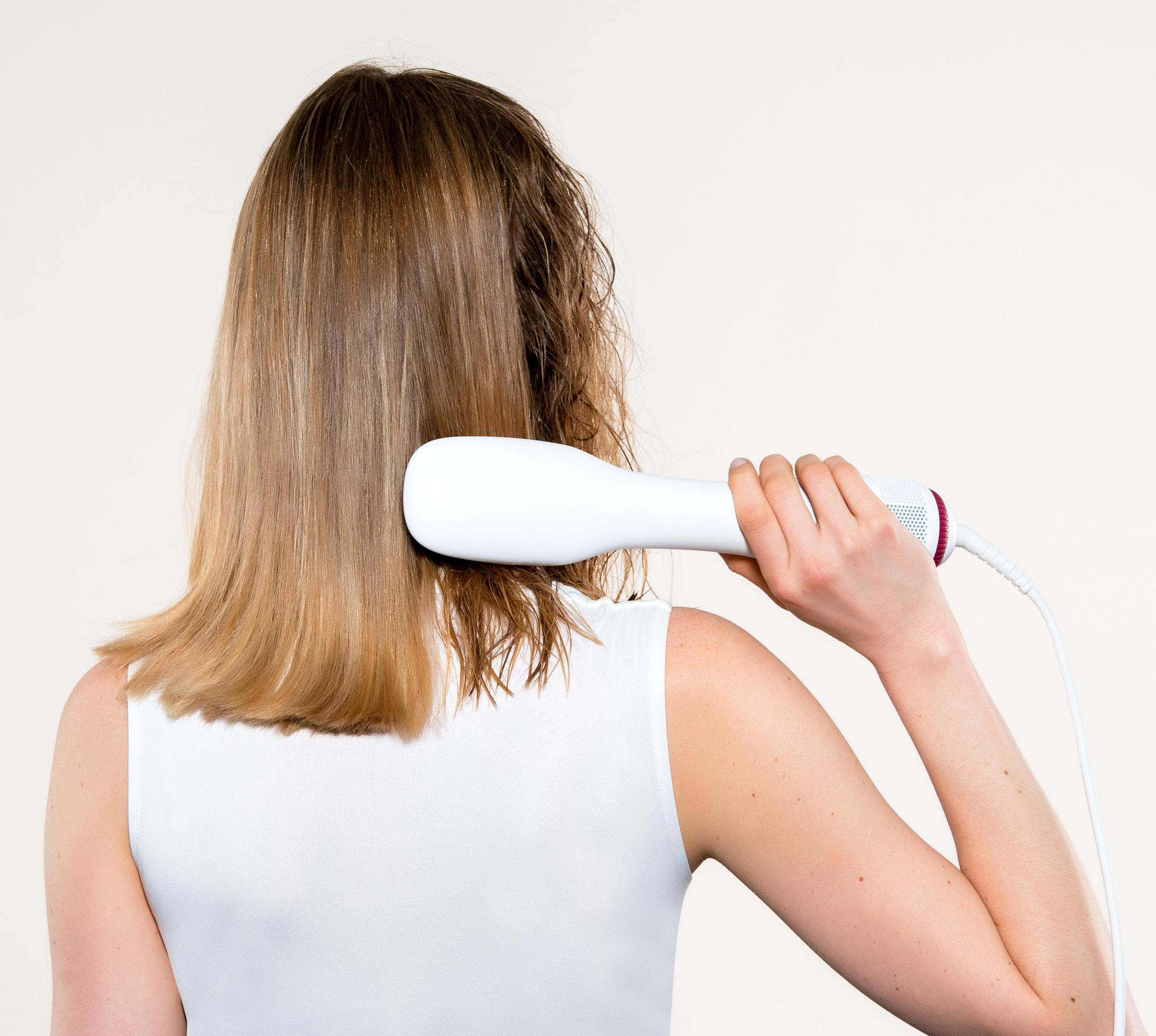 Una mujer se seca el pelo castaño mojado con un secador blanco.